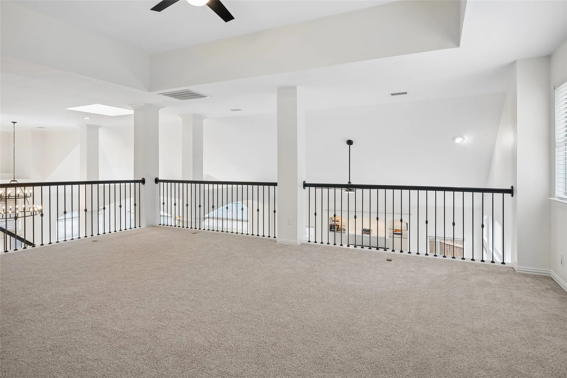 Expansive carpeted loft with an open concept design, featuring a contemporary ceiling fan, skylight, and white window blinds