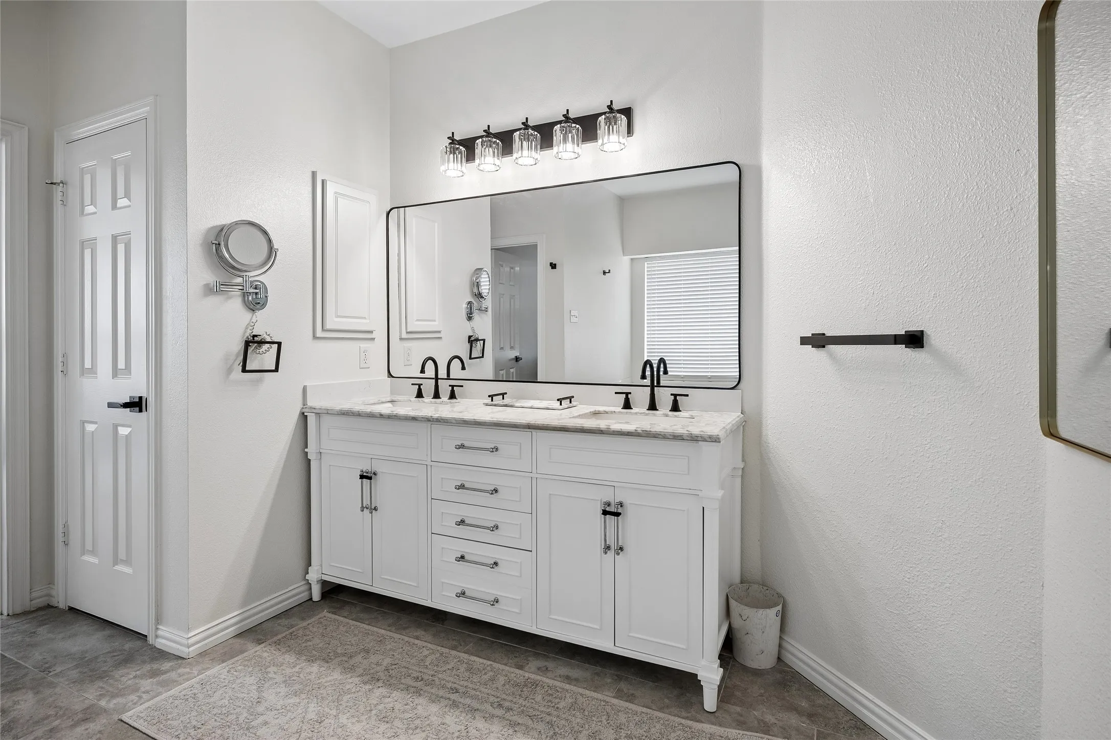 Dual vanity with white cabinetry, stone countertop, matte black fixtures, and a large framed mirror