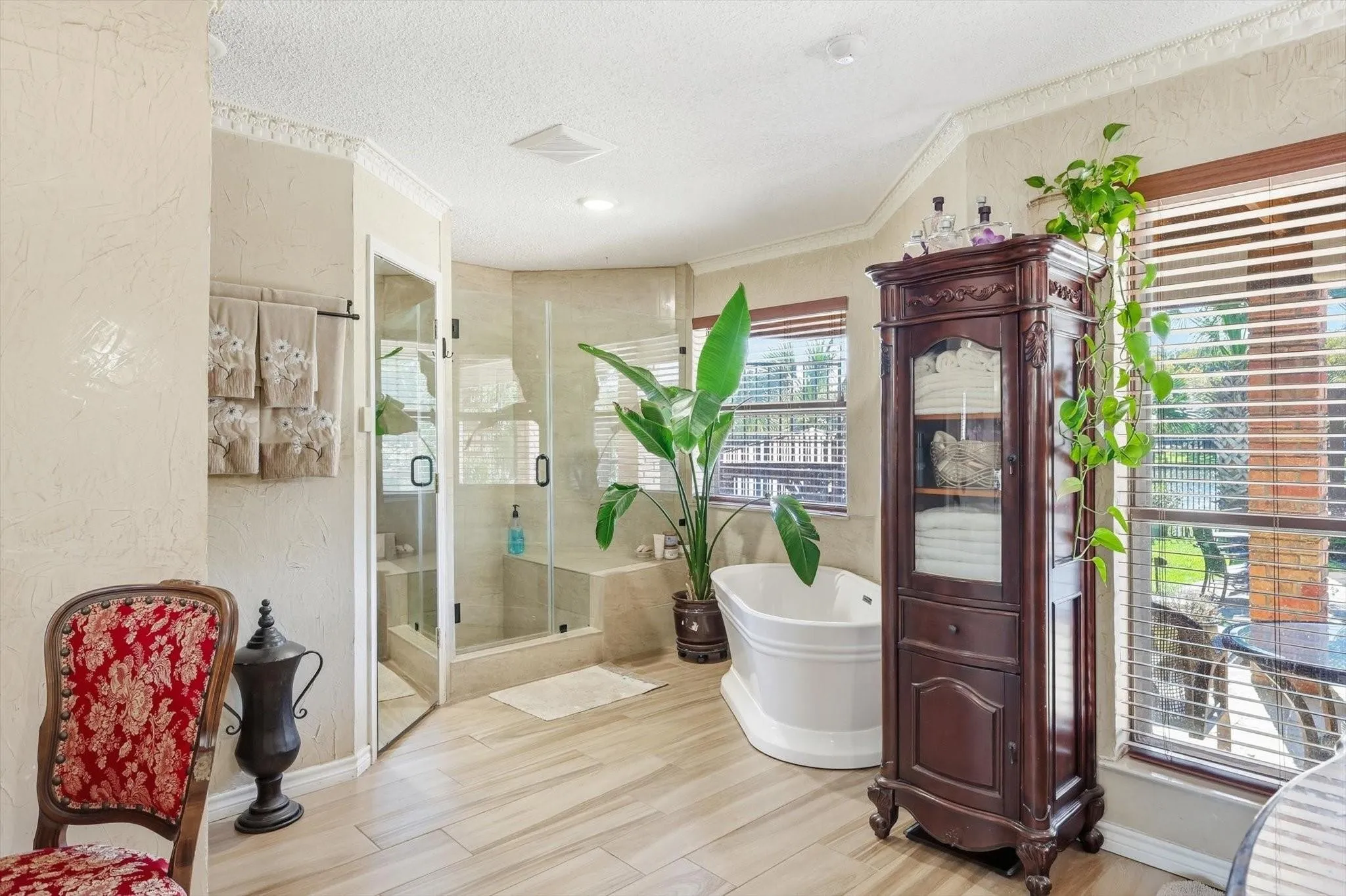 Freestanding soaking tub, walk-in shower with bench seating, large windows with blinds, crown molding, and wood-finish flooring