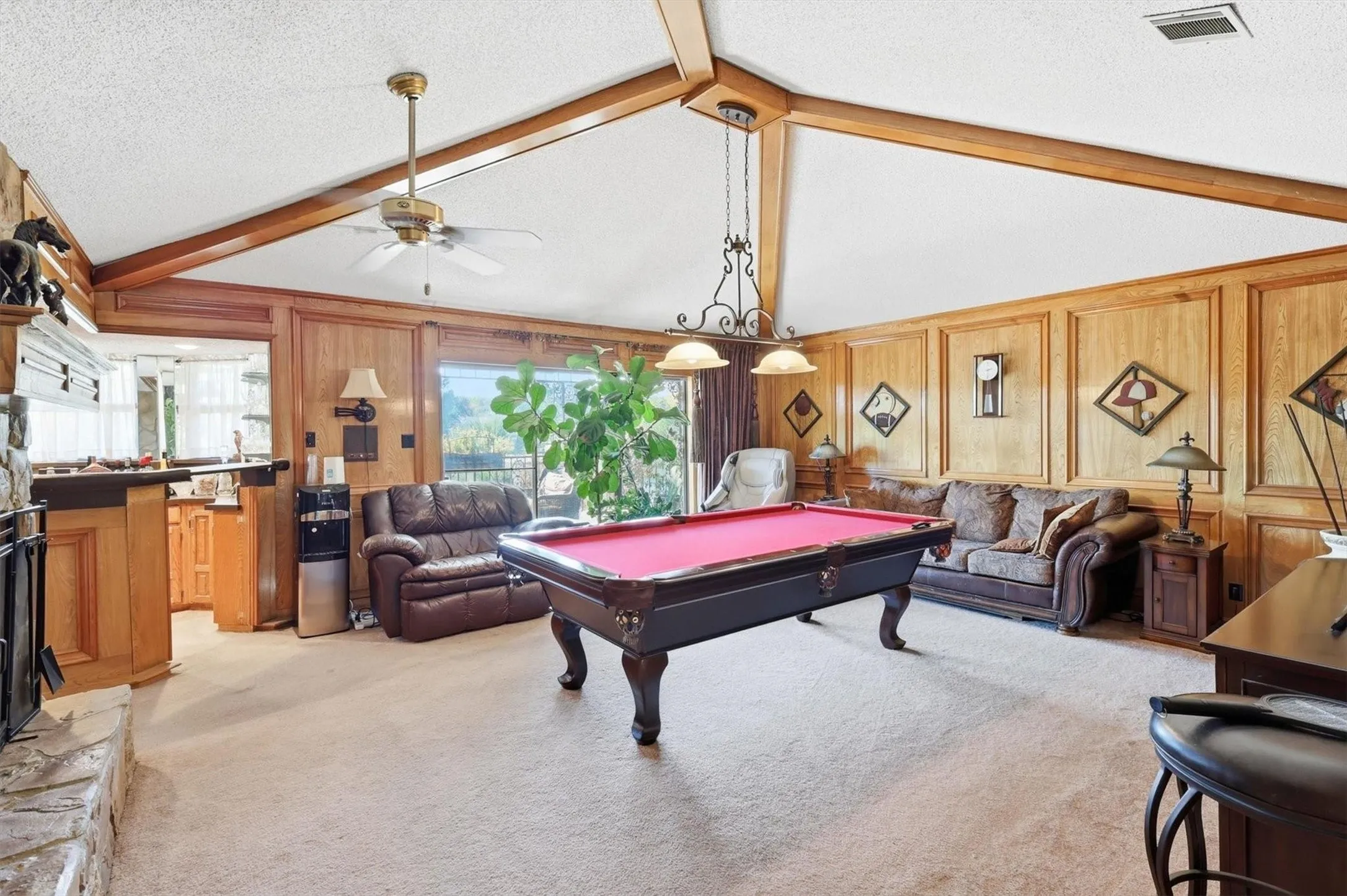 Vaulted ceiling with wood beams, wood paneling, stone fireplace, and built-in wet bar