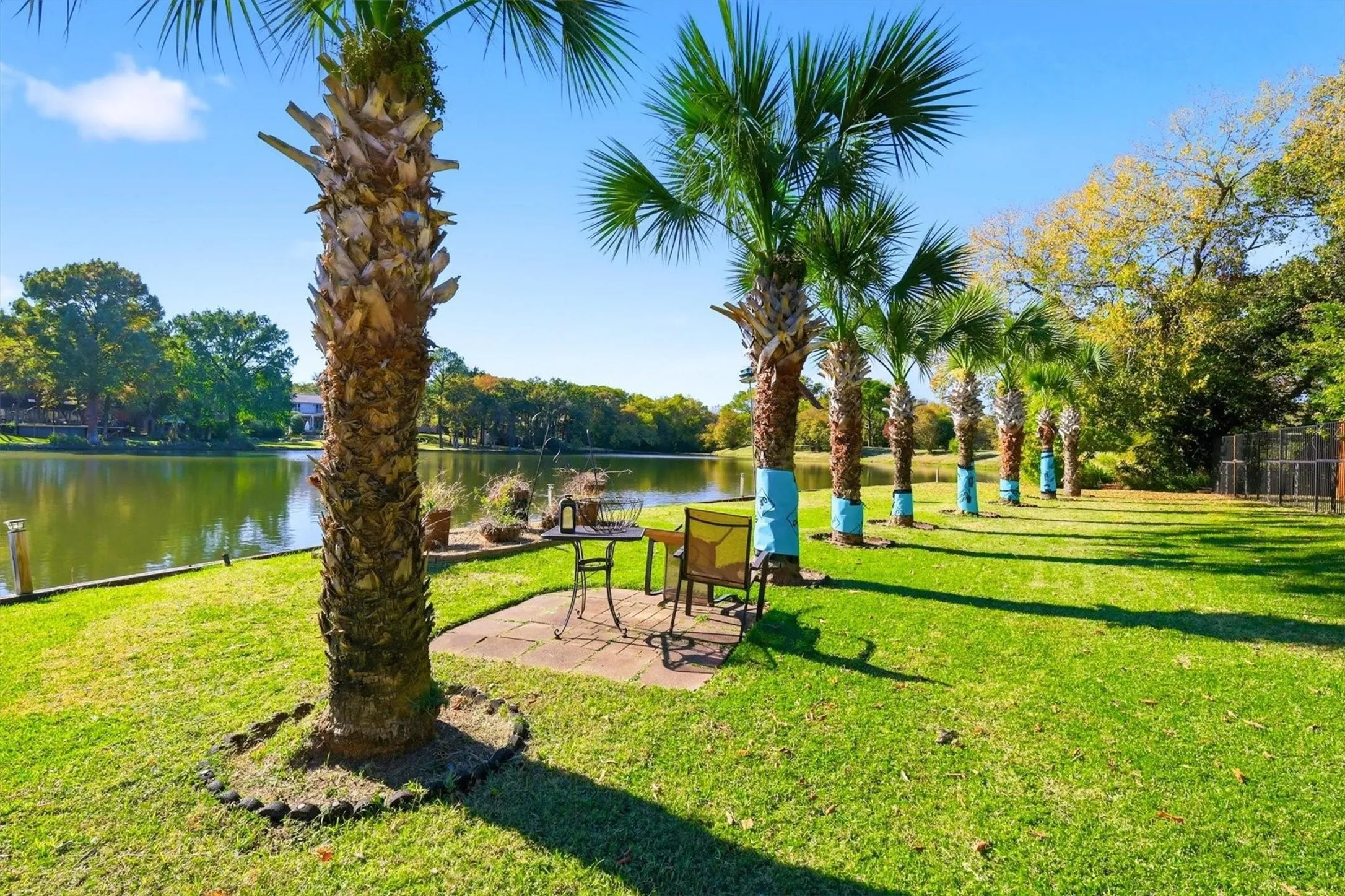 Expansive green lawn with a tree-lined perimeter, waterfront access, and a stone-paved patio area