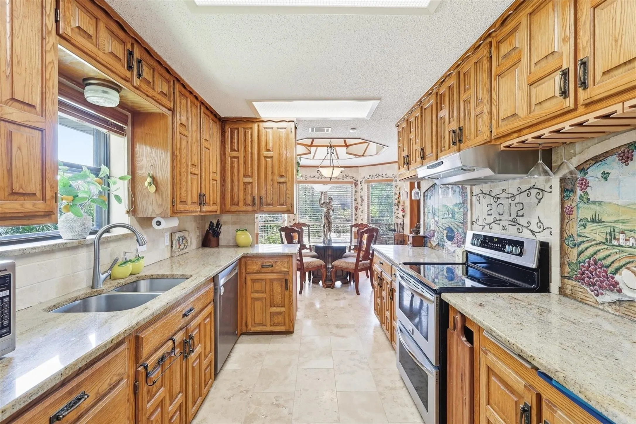 Galley kitchen featuring wood cabinetry, stone countertops, a double basin stainless steel sink, and a built-in electric range with a double oven