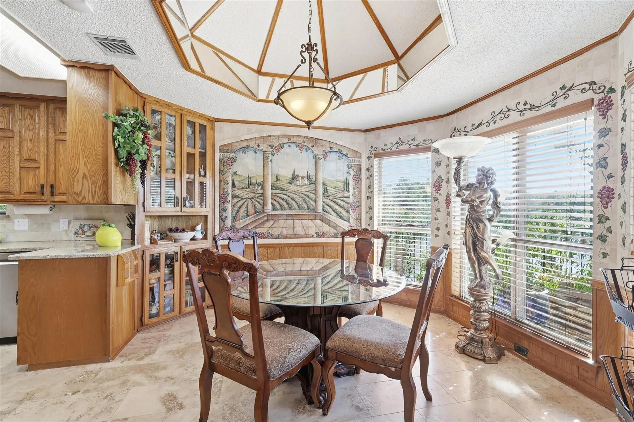 Recessed ceiling with decorative trim, kitchen cabinetry with glass-front uppers, light-toned backsplash, granite-style countertops, and tiled flooring
