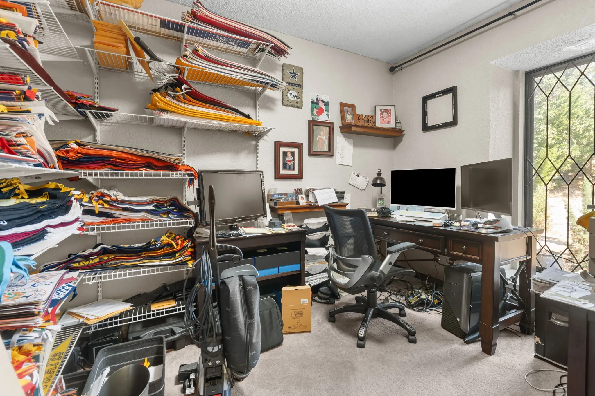 Wall-mounted shelving system, carpeted flooring, large window with decorative grilles, and built-in desk area