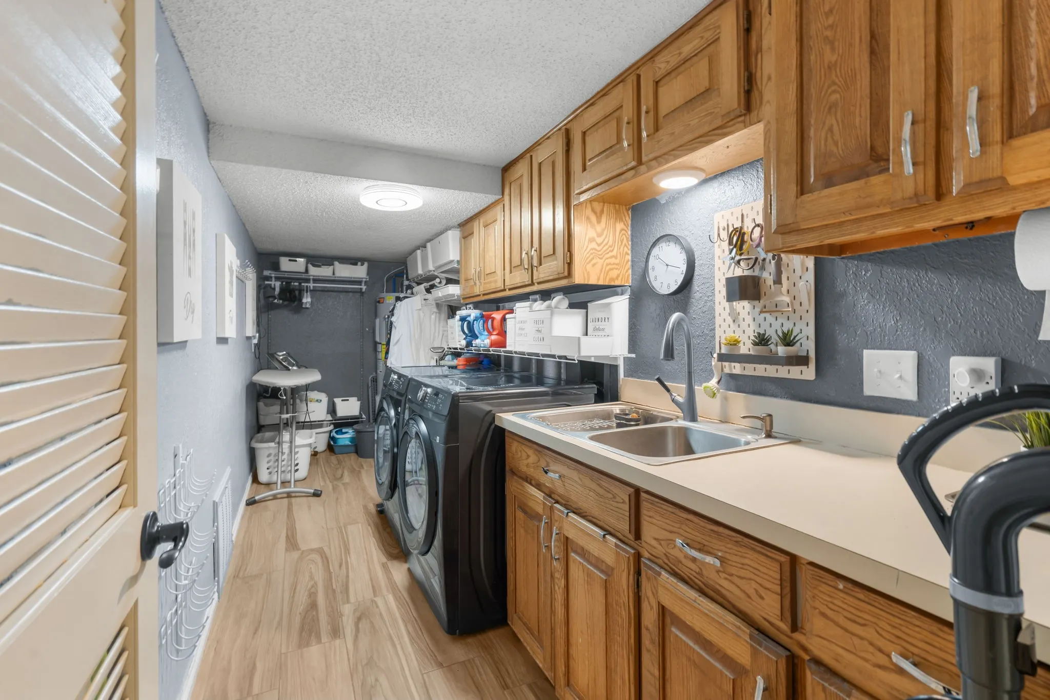 Laundry area with wood-finish flooring, wood cabinetry, built-in sink, and integrated overhead lighting
