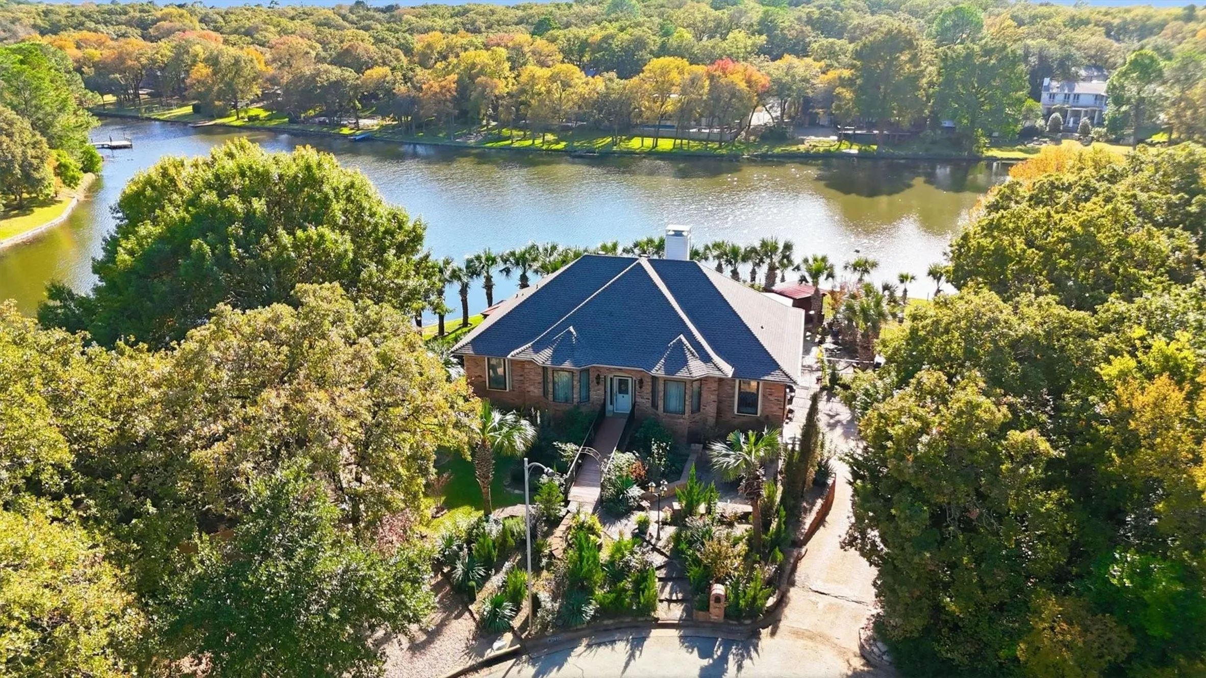 Waterfront property featuring extensive perimeter landscaping, mature trees, and a private dock