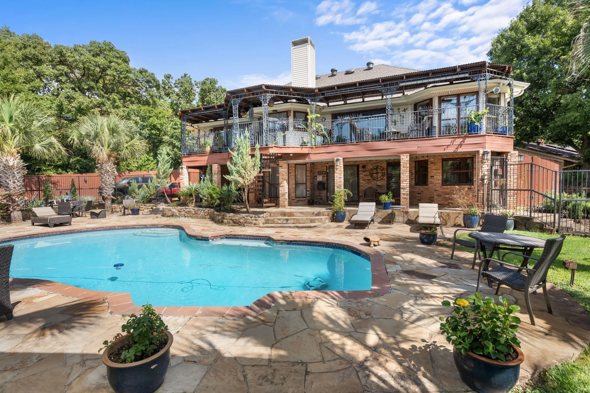 Outdoor pool with flagstone decking, a brick exterior, a second-story balcony with metal railings, and a covered patio area