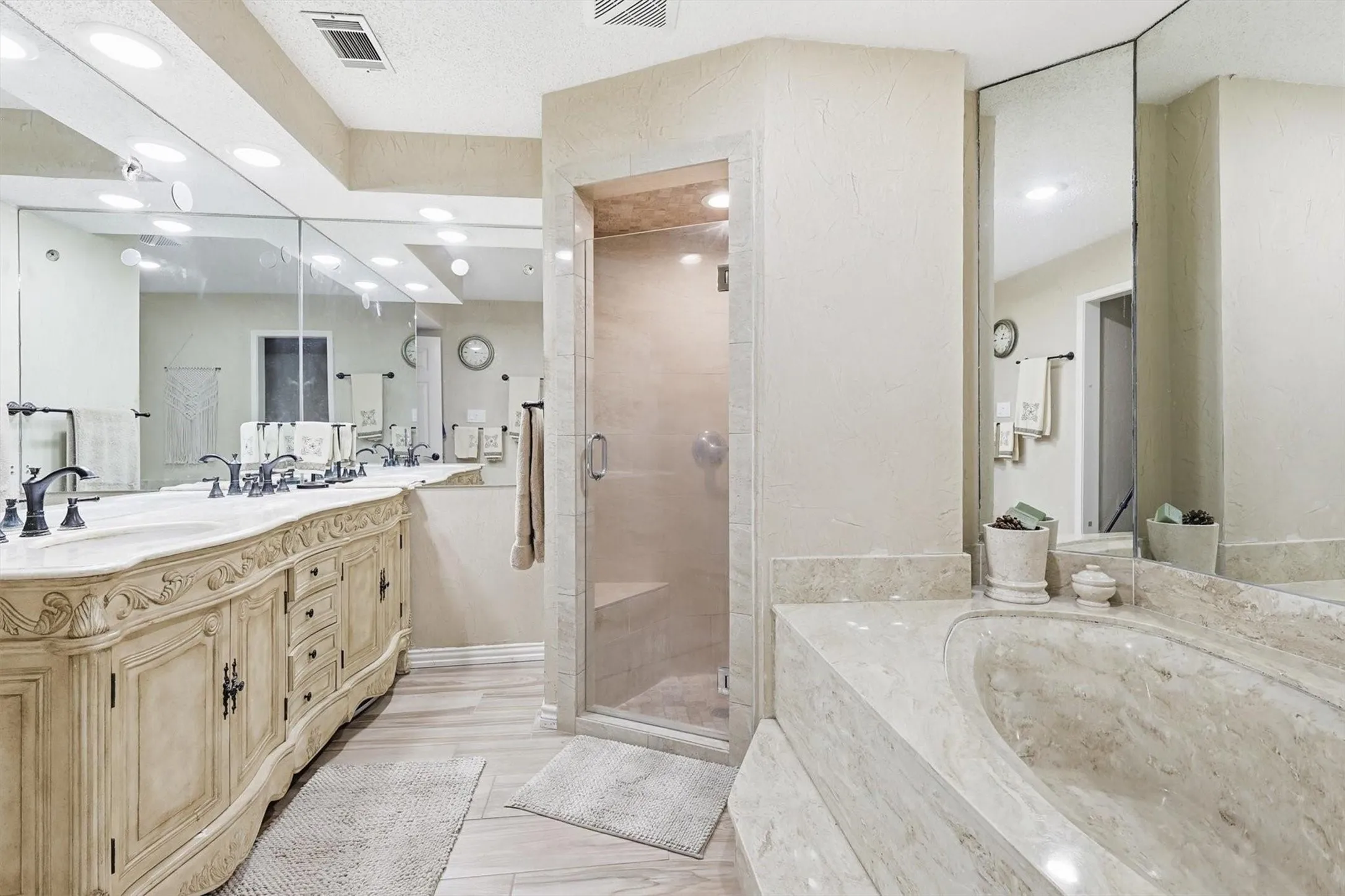 Dual vanity with integrated sinks, full-height wall mirrors, built-in soaking tub, and enclosed shower with glass door