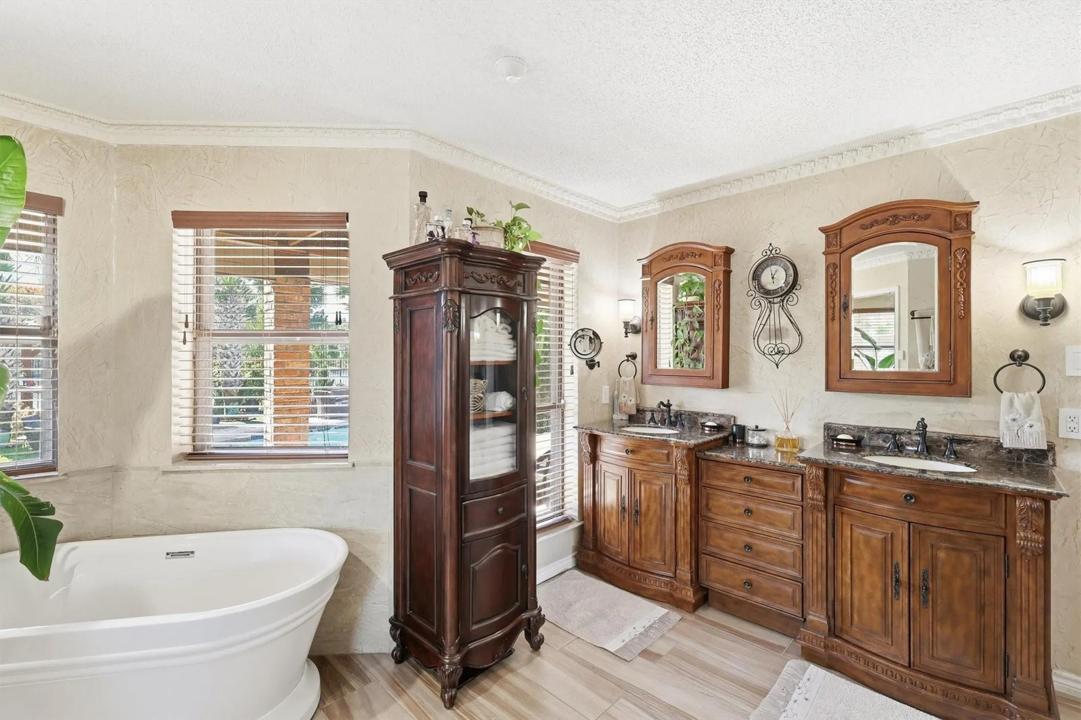 Freestanding soaking tub, wood-finish flooring, dual vanity with granite countertops, wood-framed mirrors, and custom cabinetry