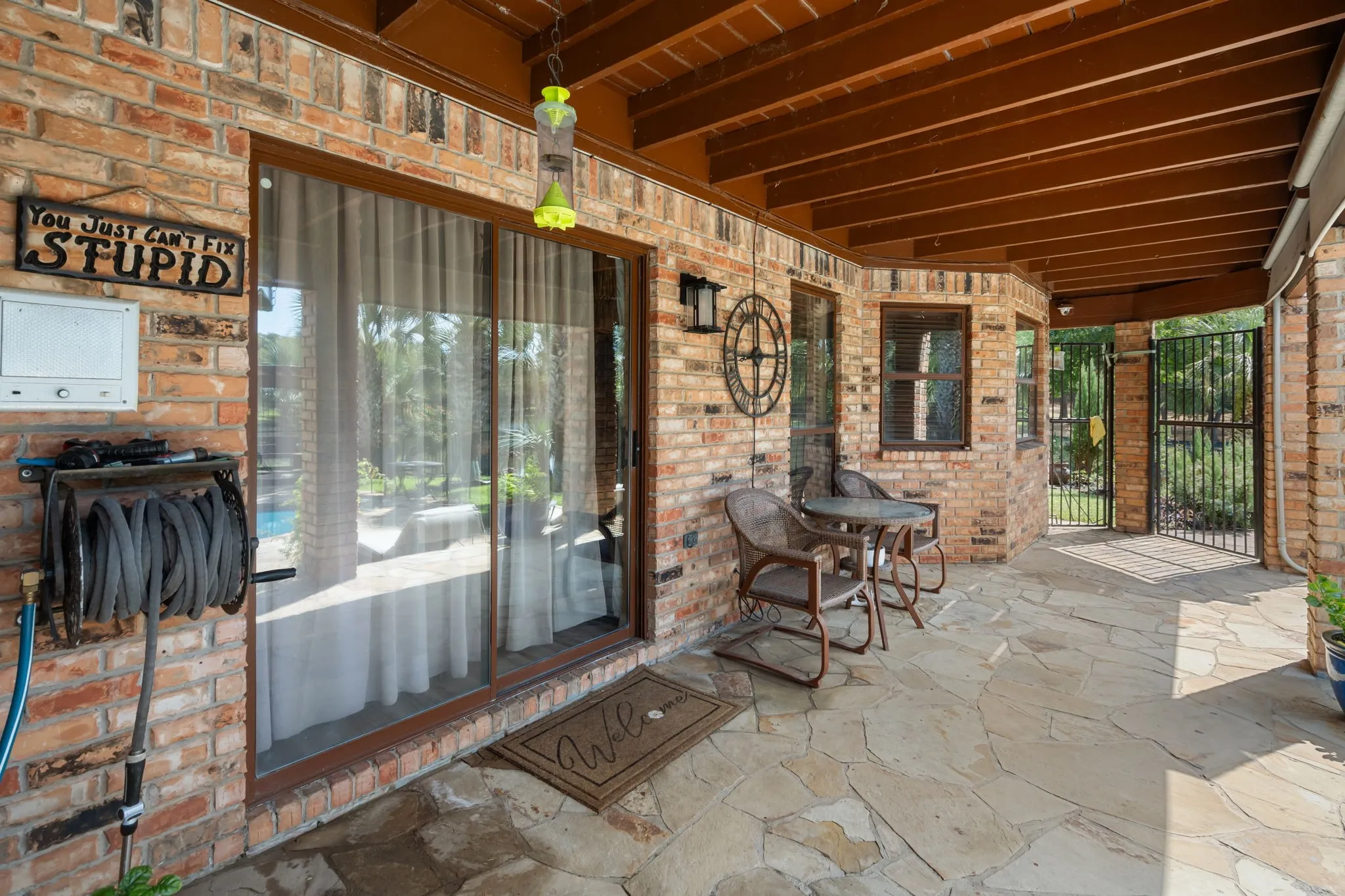 Covered patio featuring brick construction, a stone-paved surface, and exposed wood beam ceiling