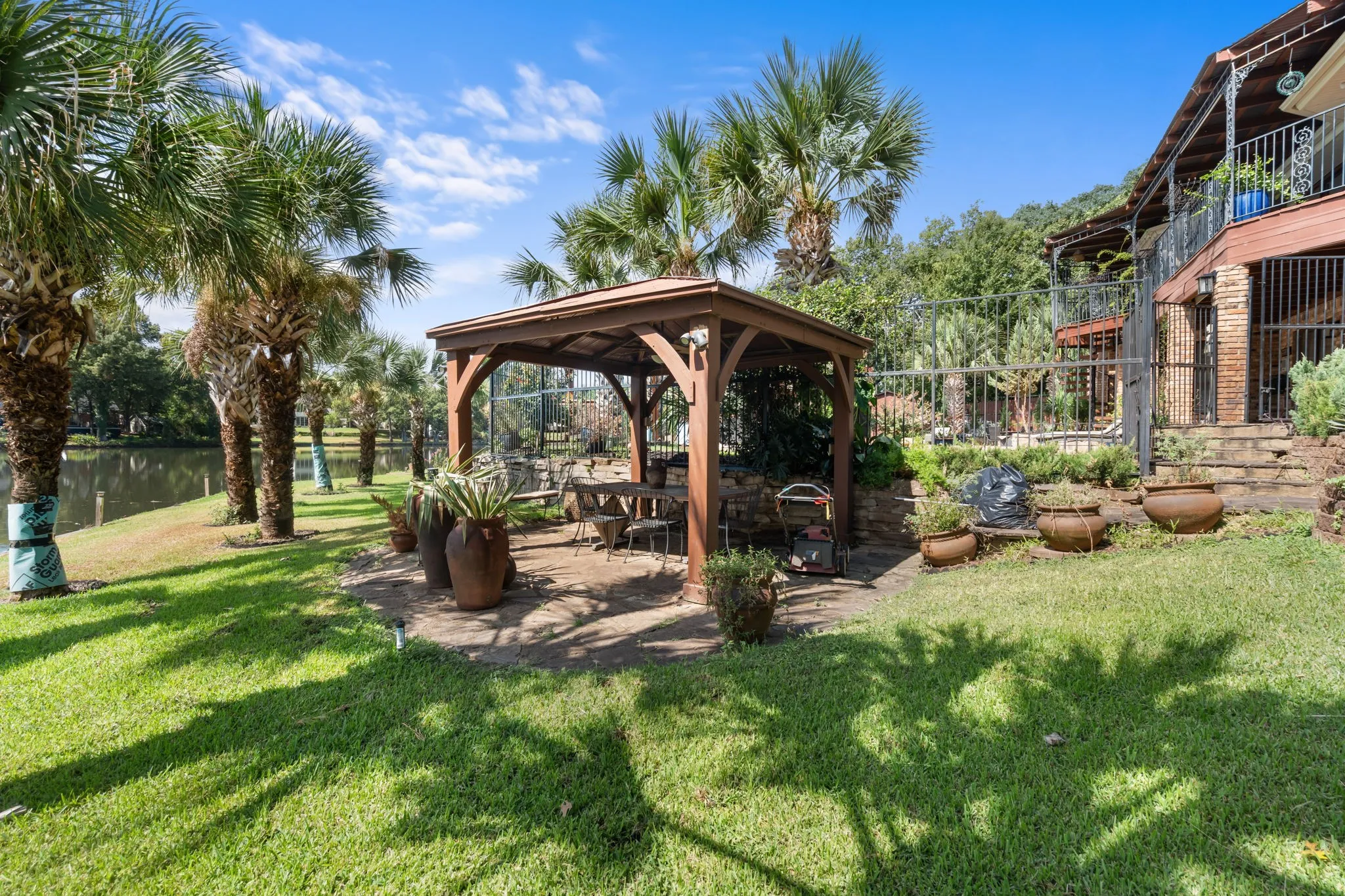 Expansive lawn area with a built-in gazebo, numerous palm trees, and water frontage