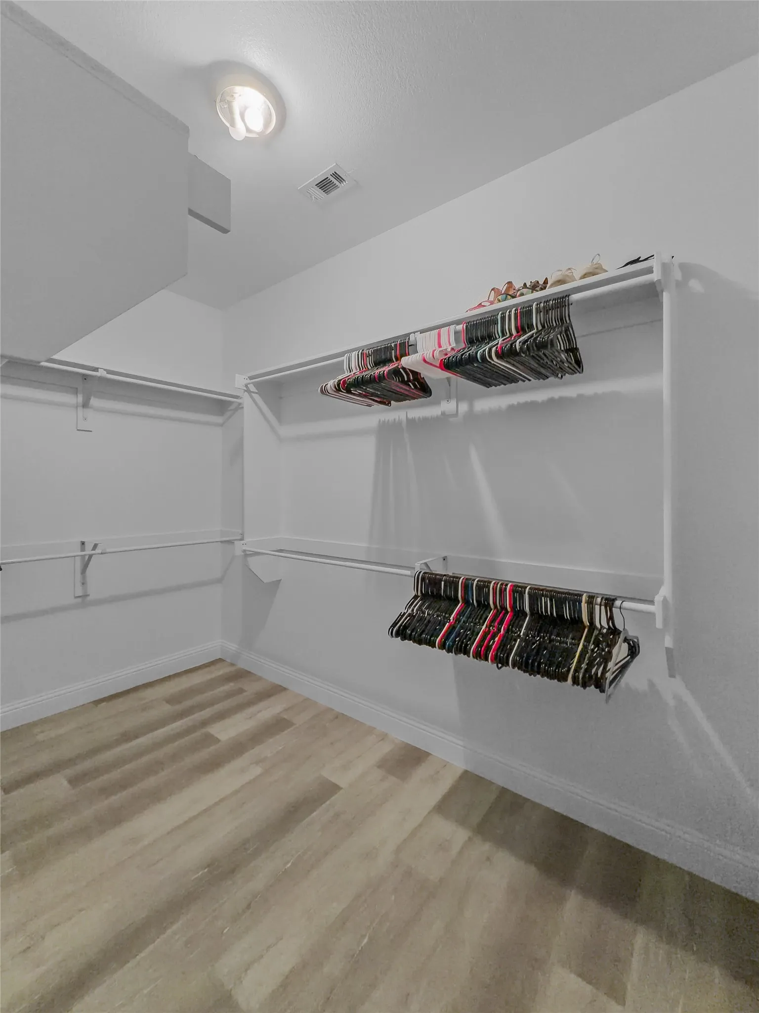 Walk-in closet featuring wood-finish flooring, white walls, built-in shelving, and hanging rods
