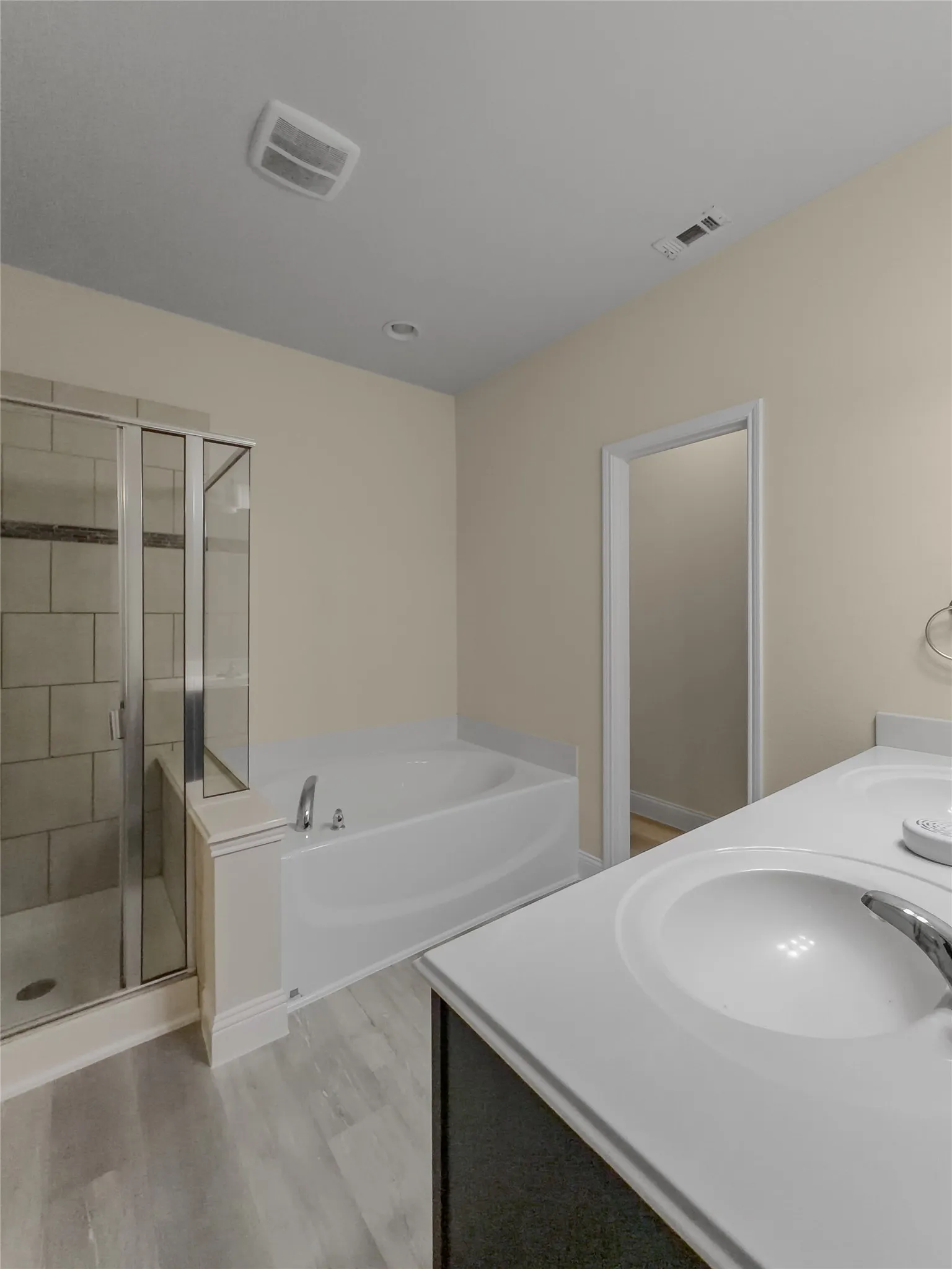 Dual vanity with integrated sinks, built-in bathtub, glass-enclosed shower with tiled walls, and wood-finish flooring