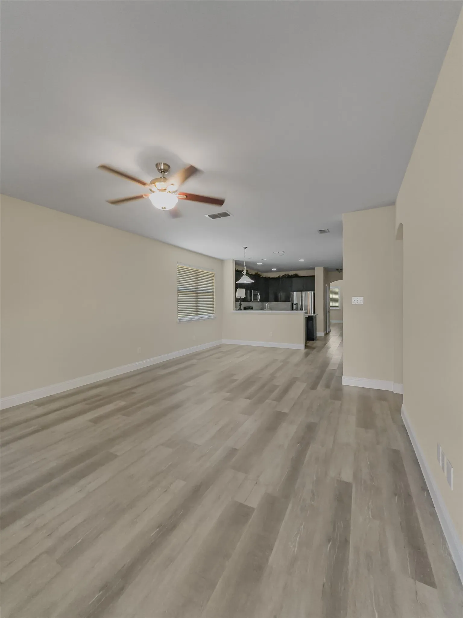 Spacious room featuring wood-finish flooring, a ceiling fan with integrated lighting, and neutral wall tones