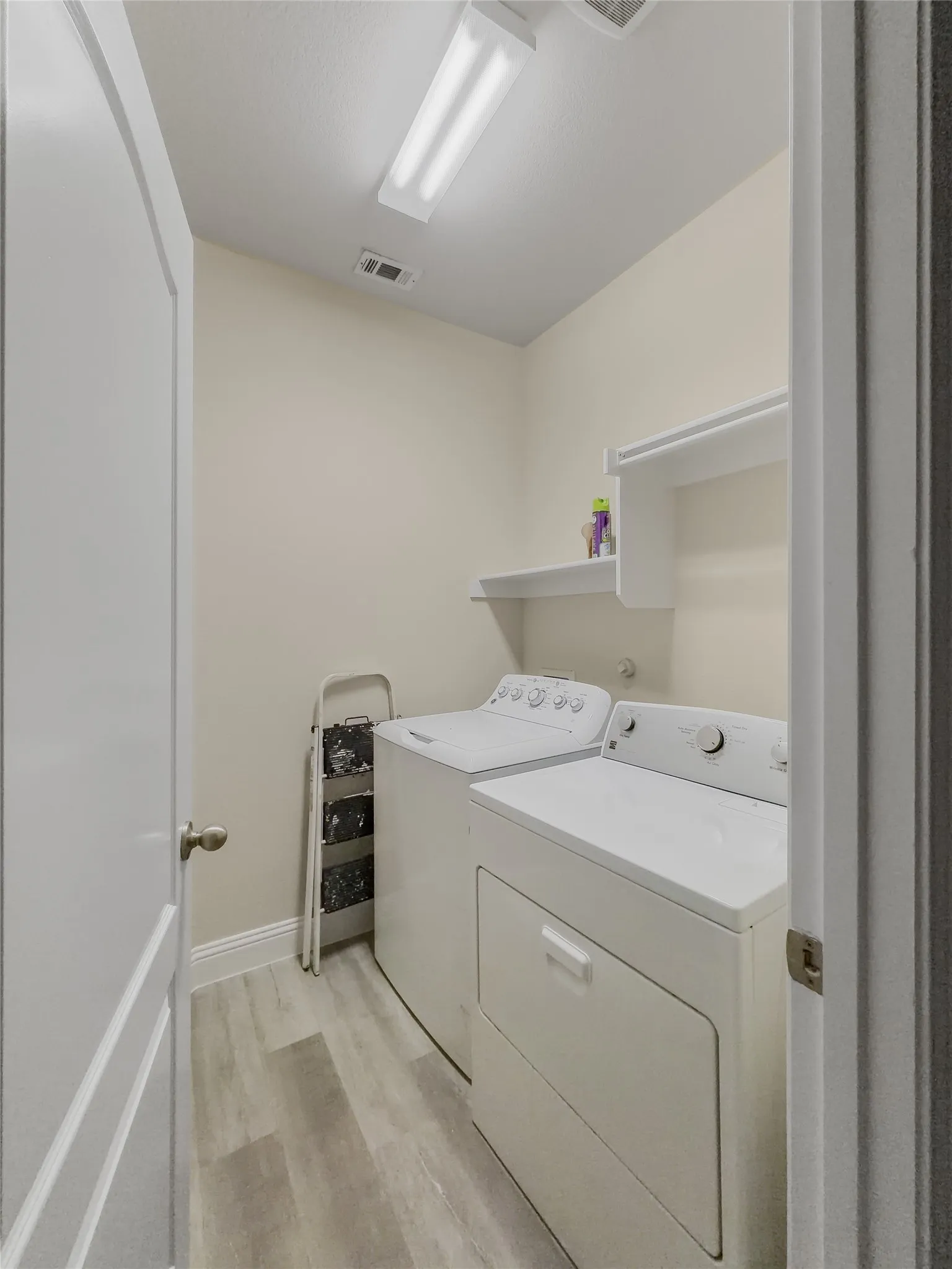 Laundry room with wood-finish flooring, built-in shelving, and a ceiling-mounted fluorescent light fixture