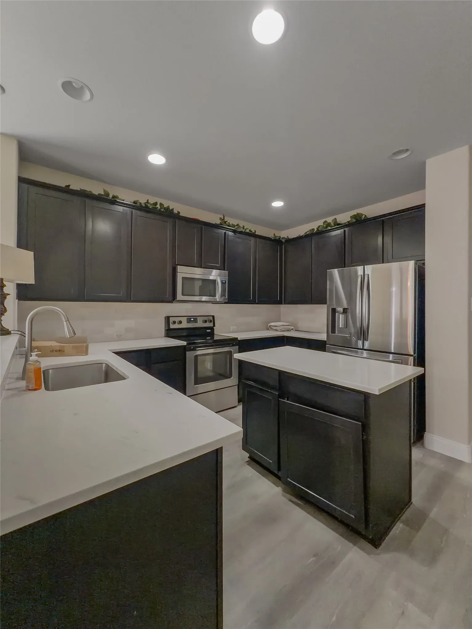 Kitchen featuring dark cabinetry, light countertops, stainless steel appliances, a center island, and wood-finish flooring