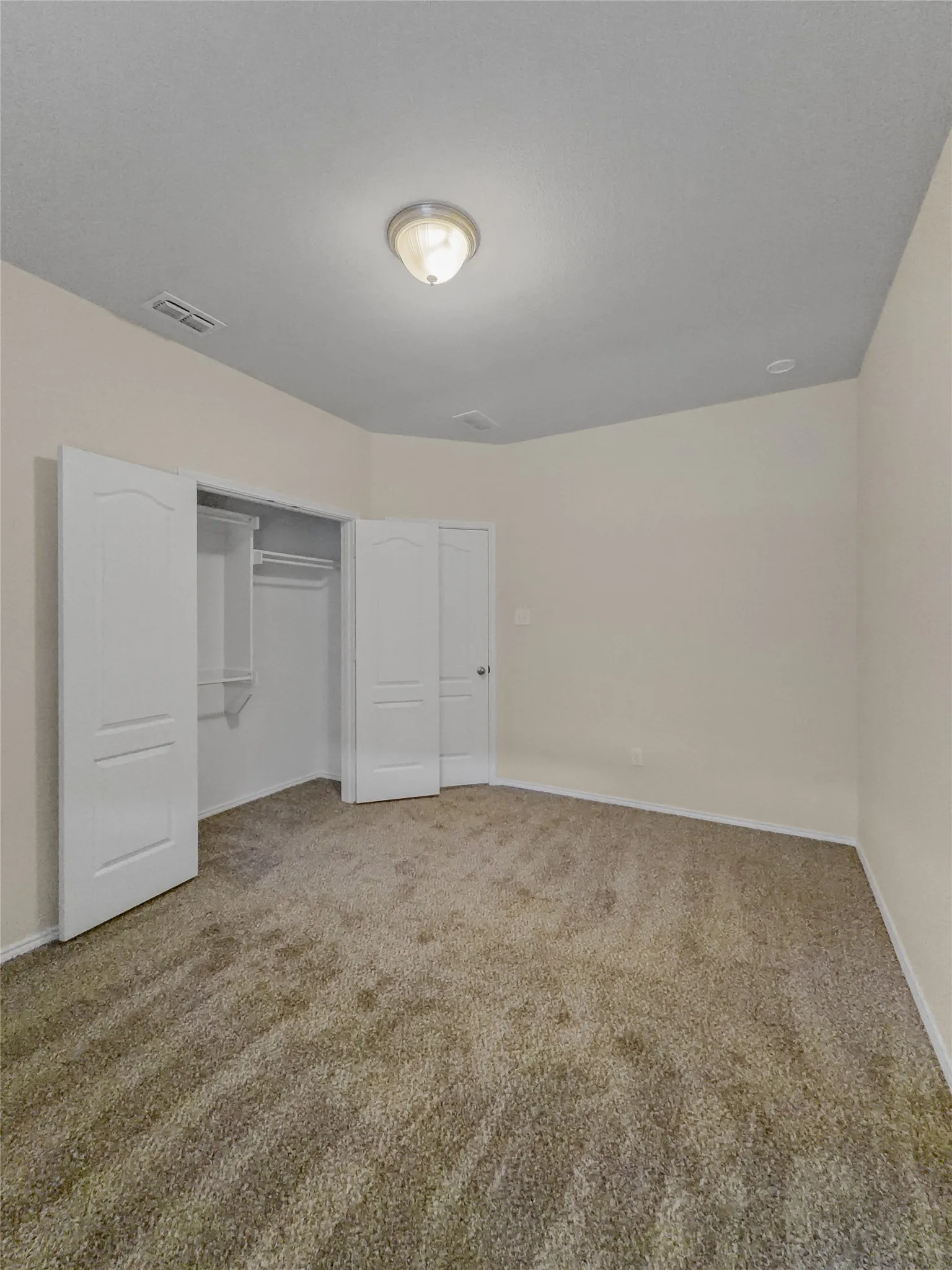 Neutral-toned wall-to-wall carpeting with a flush-mount ceiling light fixture, and a built-in closet with bi-fold doors