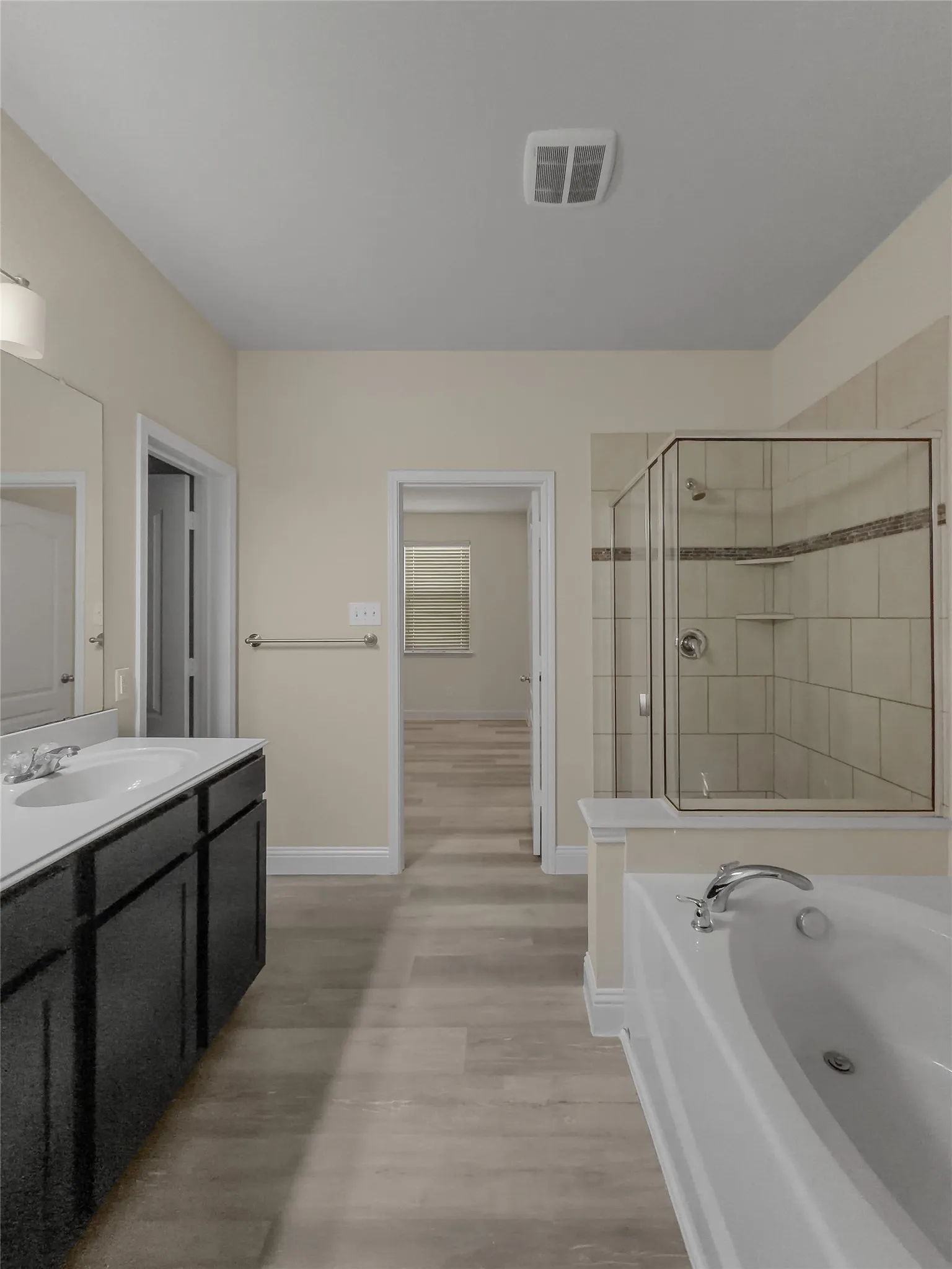 Dual vanity with undermount sinks, walk-in shower with glass enclosure, separate soaking tub, and wood-finish flooring
