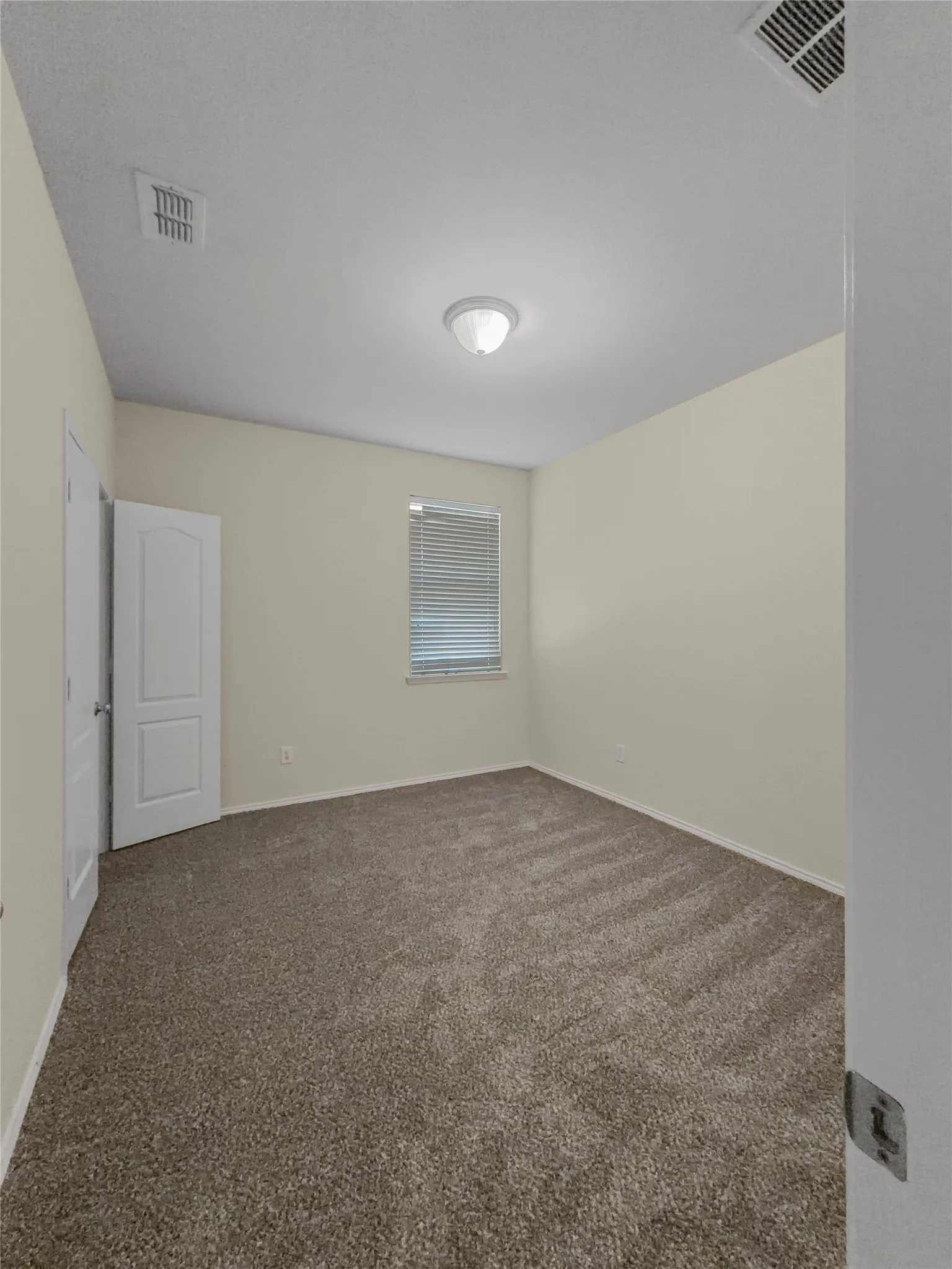 Carpeted room with neutral wall tones and a window featuring blinds