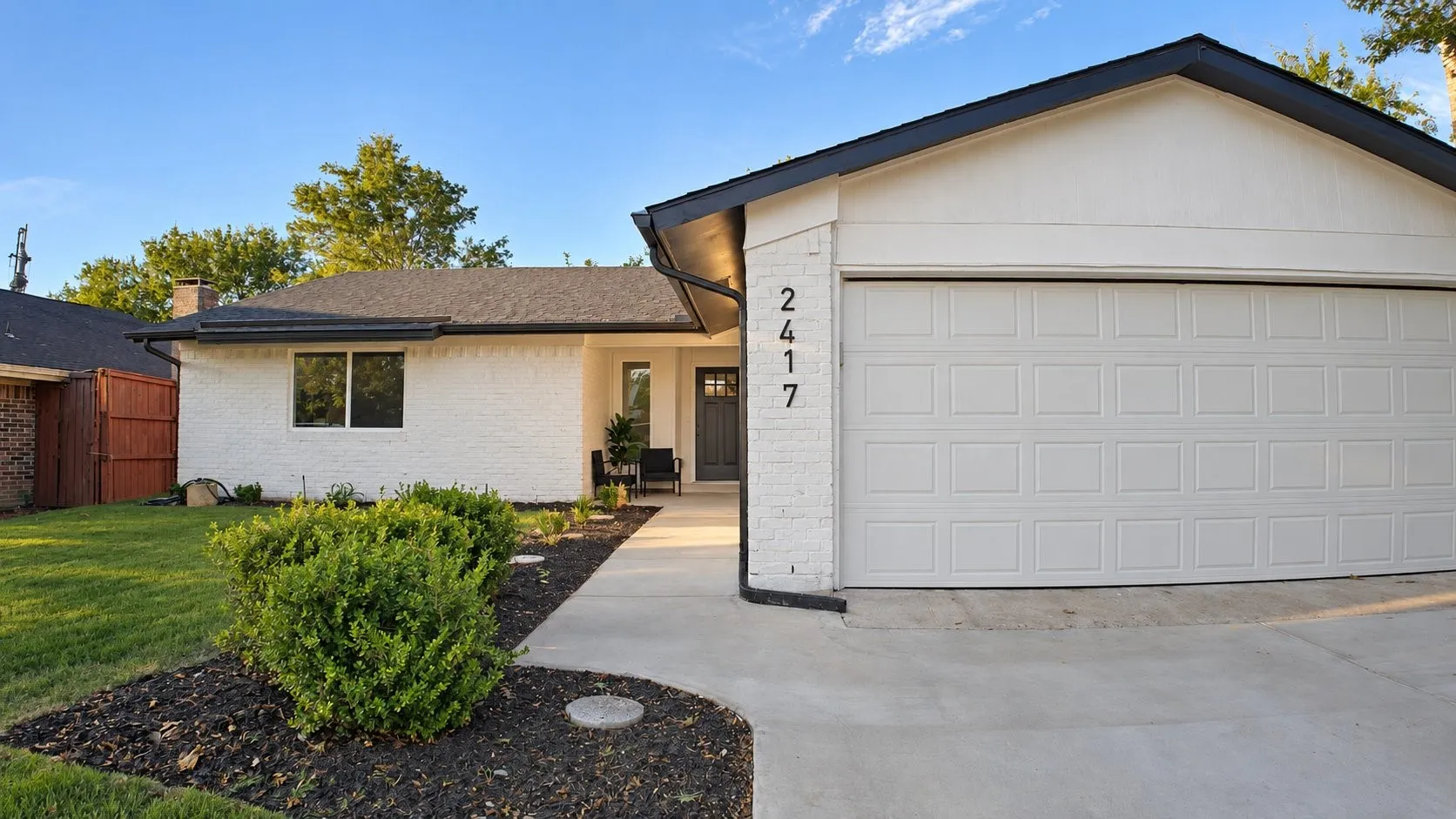White brick exterior with black trim, a paneled garage door, a concrete driveway, and a front walkway