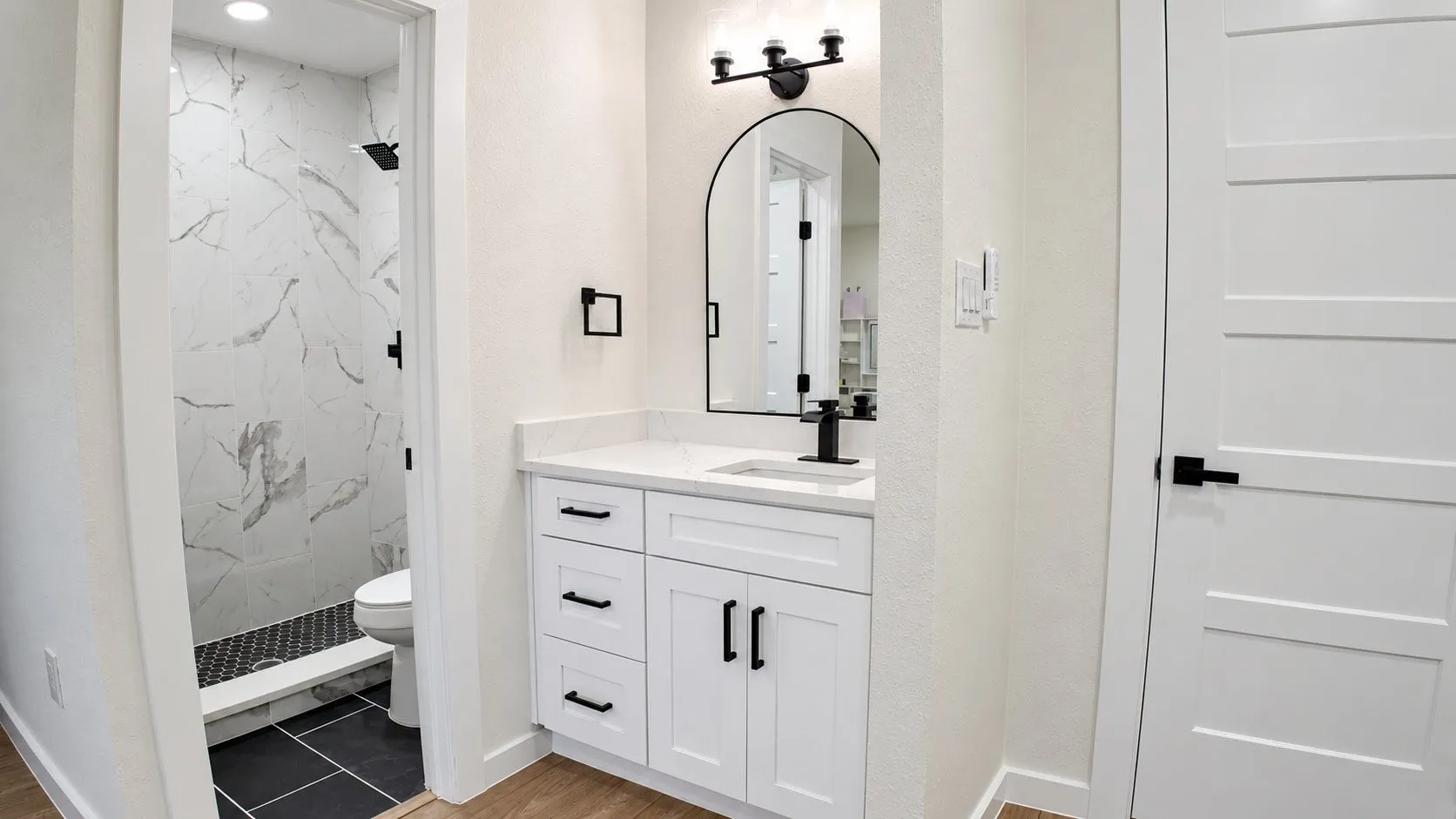 White vanity with black hardware, arched mirror, black faucet, and white countertop