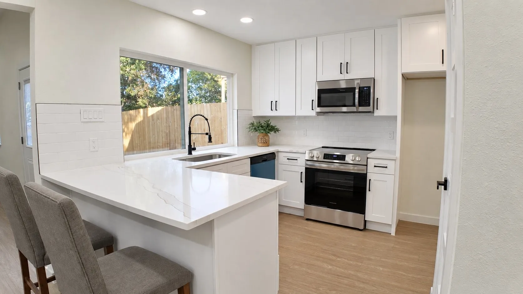 White cabinetry with matte black hardware, stainless steel appliances, white subway tile backsplash, and light wood-finish flooring