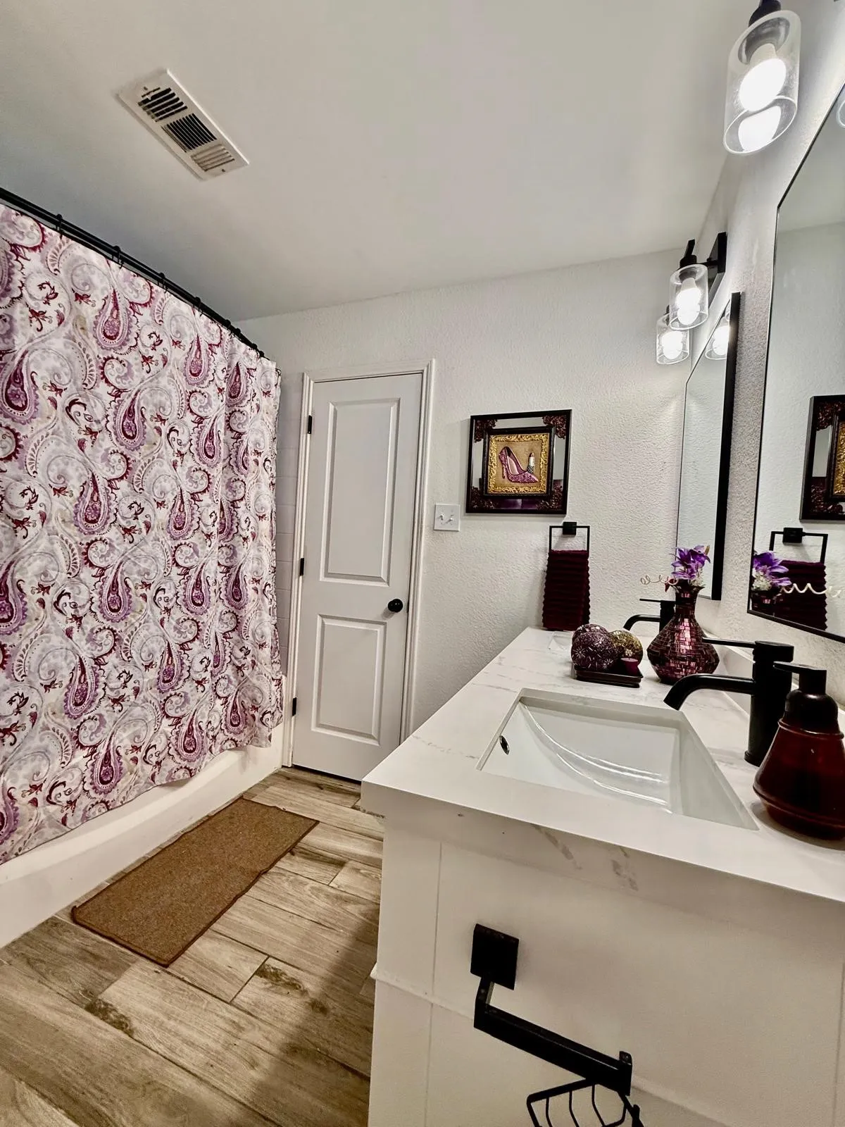 Vanity with integrated sink, stone-finish countertop, black hardware, wood-finish flooring, and wall-mounted light fixtures