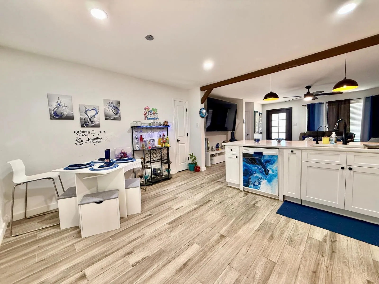 Wood-finish flooring throughout, white kitchen cabinetry with dark hardware, recessed lighting, and a prominent decorative beam detail