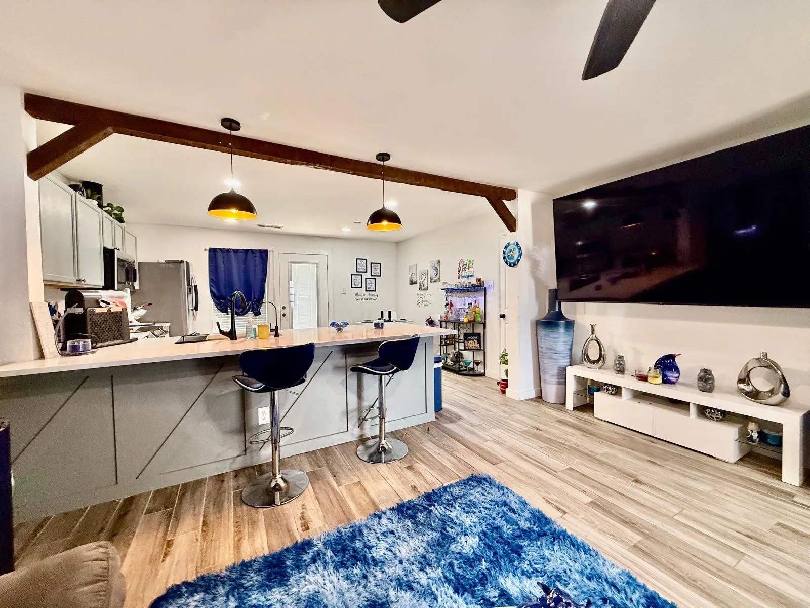 Open-concept living area with wood-finish flooring, a kitchen island with seating, a decorative exposed beam, gray cabinetry, and pendant lighting