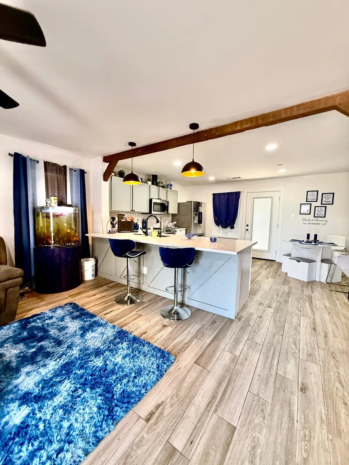 Wood-finish flooring throughout, kitchen island with seating, pendant lighting fixtures, exposed wood beam, and stainless steel appliances