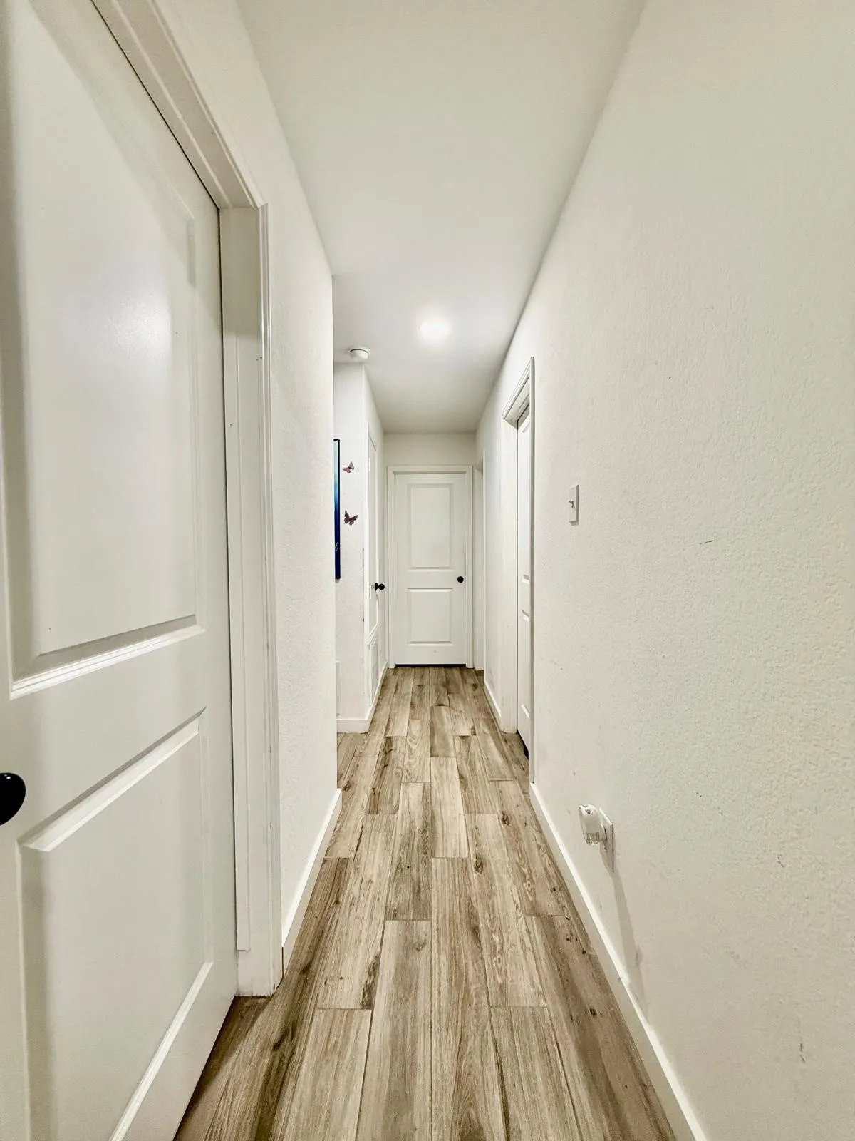 Hallway featuring wood-finish flooring, white walls, and white doors with black hardware