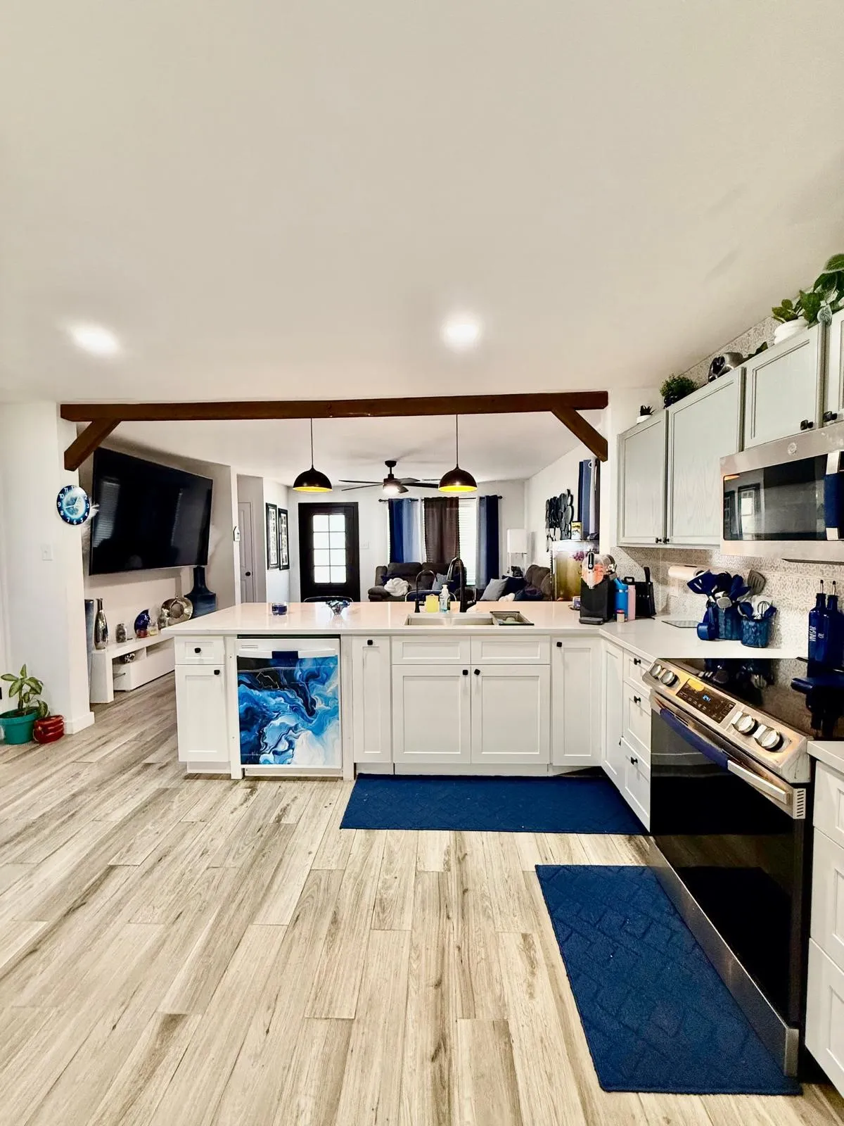 Wood-finish flooring throughout, white cabinetry with dark hardware, peninsula countertop with sink, stainless steel oven, and overhead microwave