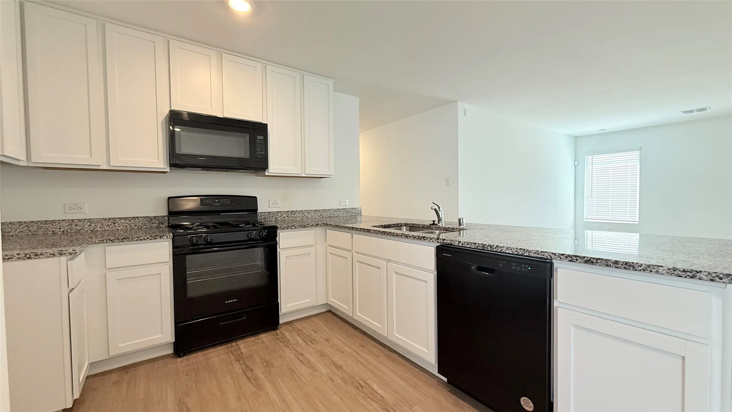 Kitchen featuring white cabinetry, granite countertops, black appliances, a built-in microwave, and wood-finish flooring