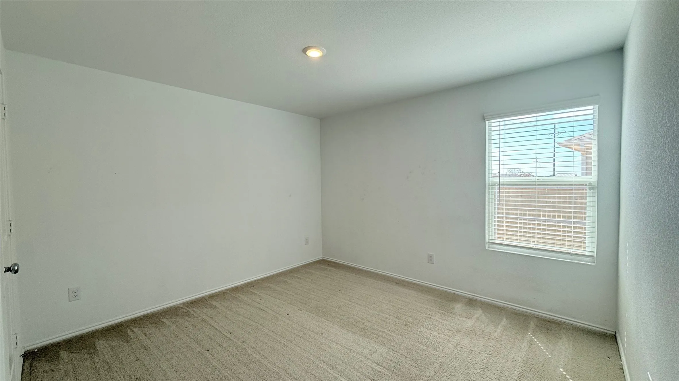 Carpeted room with white walls, a single window with blinds, and a recessed ceiling light