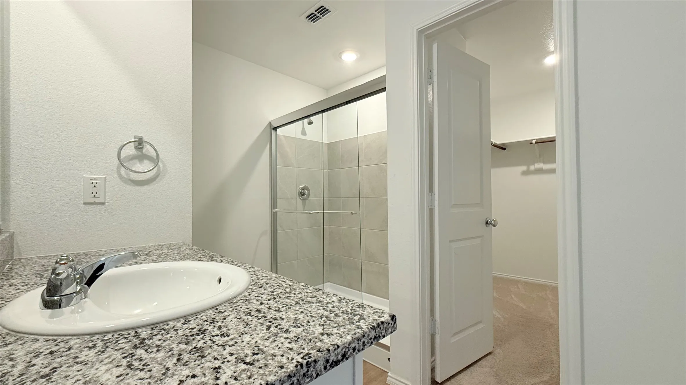 Vanity with granite-style countertop and undermount sink, chrome faucet, glass-enclosed shower with tiled walls, and recessed lighting