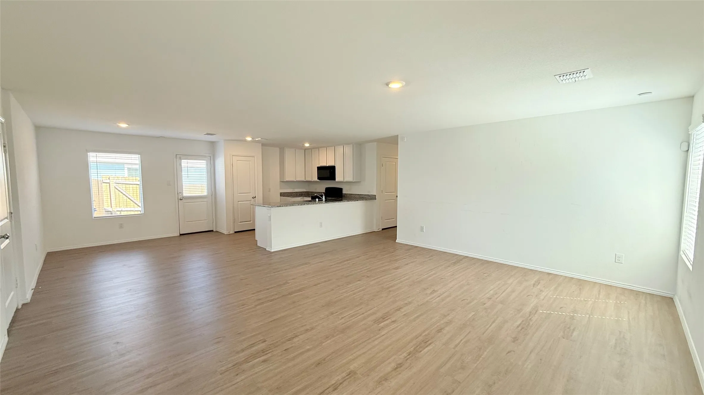 Open-concept living space with wood-finish flooring, recessed lighting, white cabinetry, and stainless steel appliances