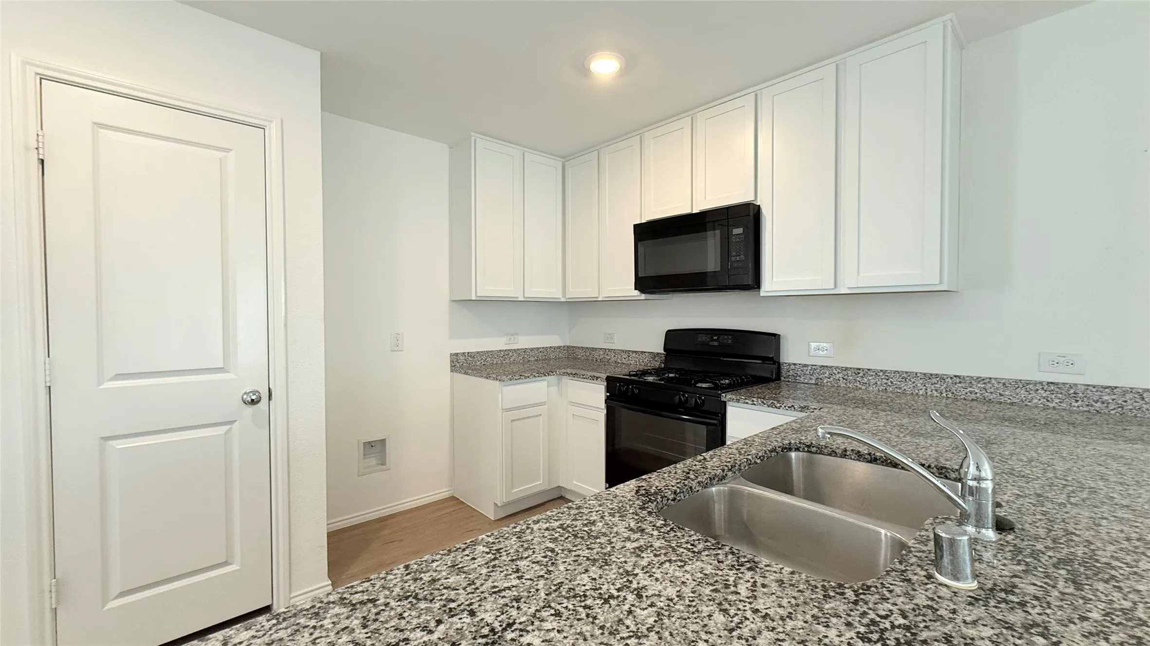 Kitchen featuring white cabinetry, stone-finish countertops, a double basin stainless steel sink, and black appliances
