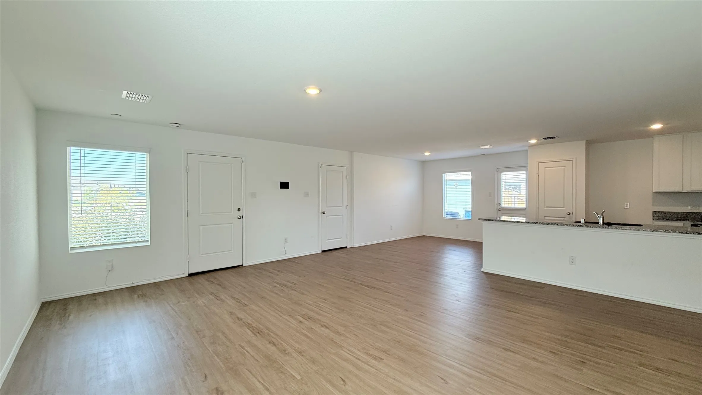 Open-concept living area featuring wood-finish flooring, recessed lighting, multiple windows, and a kitchen pass-through with a stone-look countertop