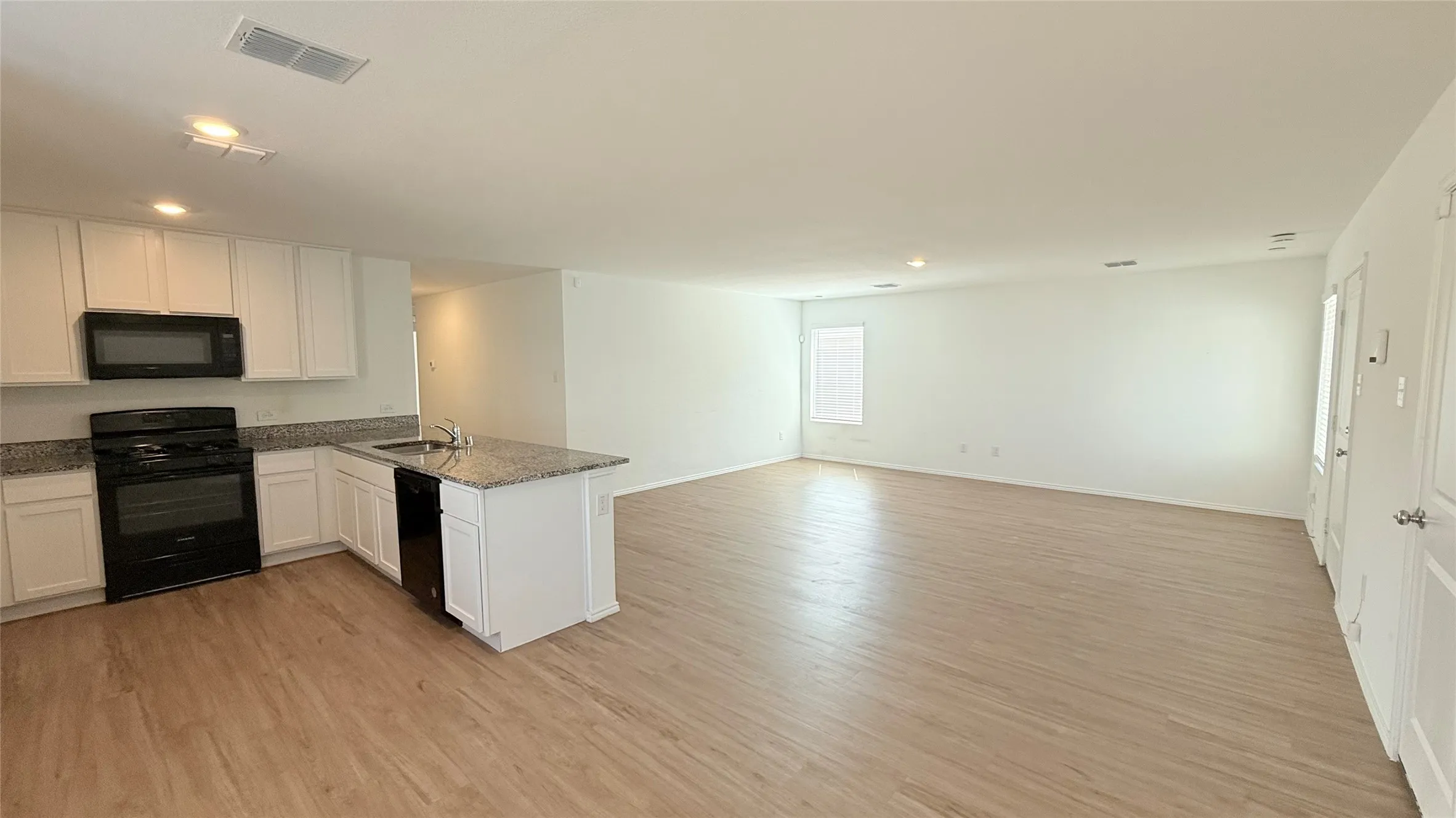 Open-concept living area featuring wood-finish flooring, white cabinetry, a kitchen island with a sink, and black appliances