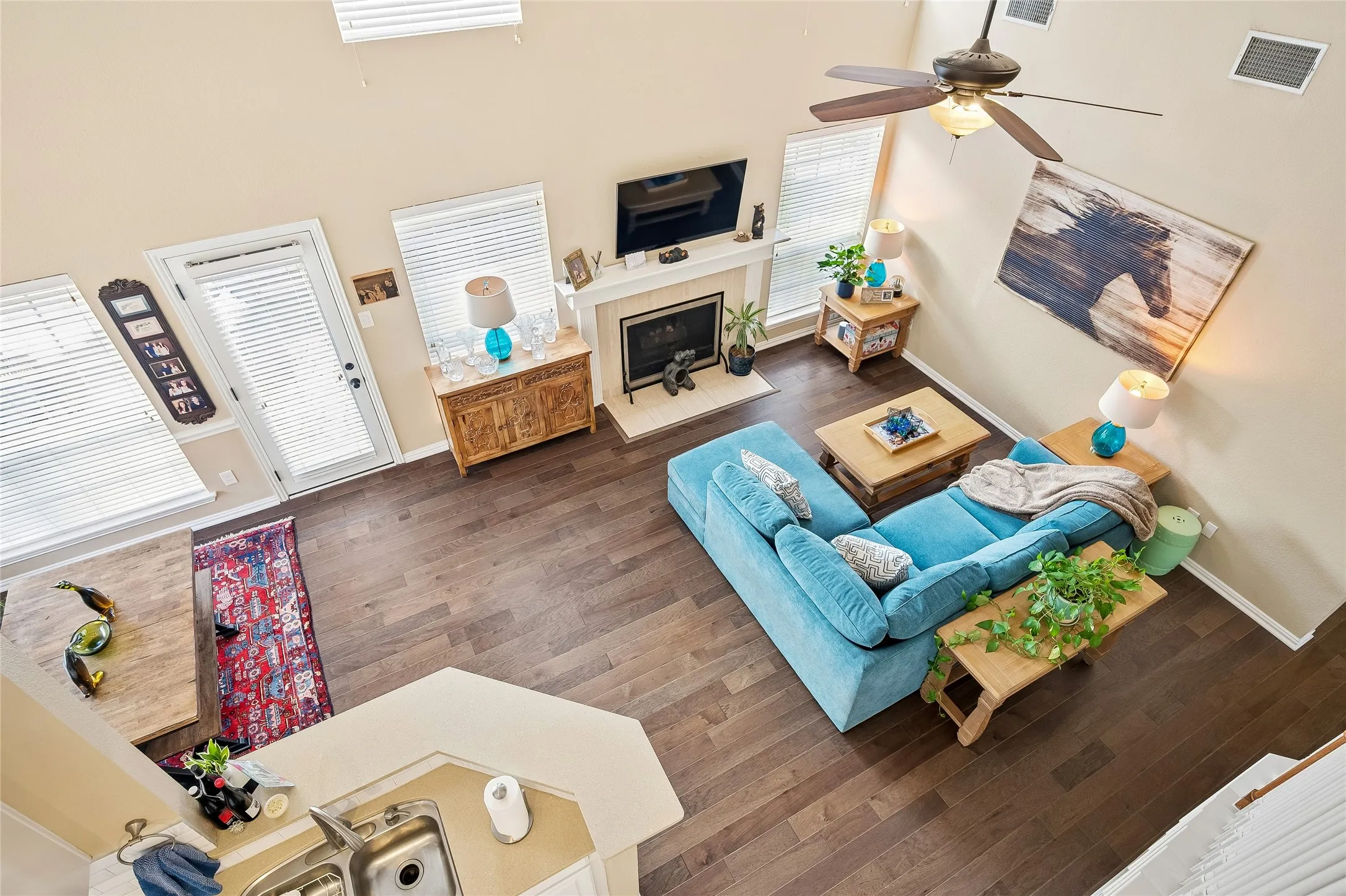 Vaulted living area featuring wood-finish flooring, a fireplace with a mantel, and multiple large windows
