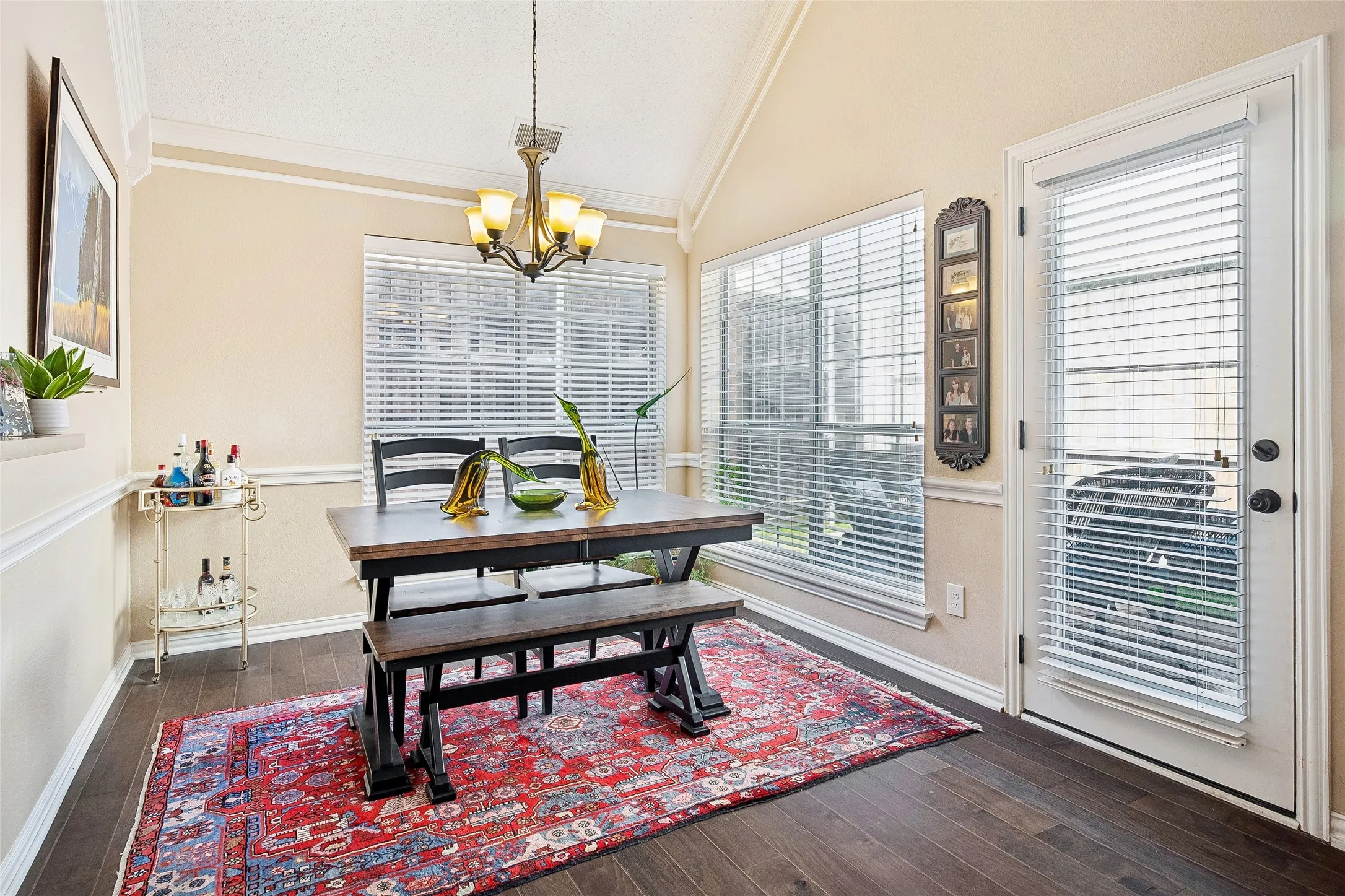 Dining area featuring dark wood-finish flooring, a vaulted ceiling, and an exterior door with integrated blinds