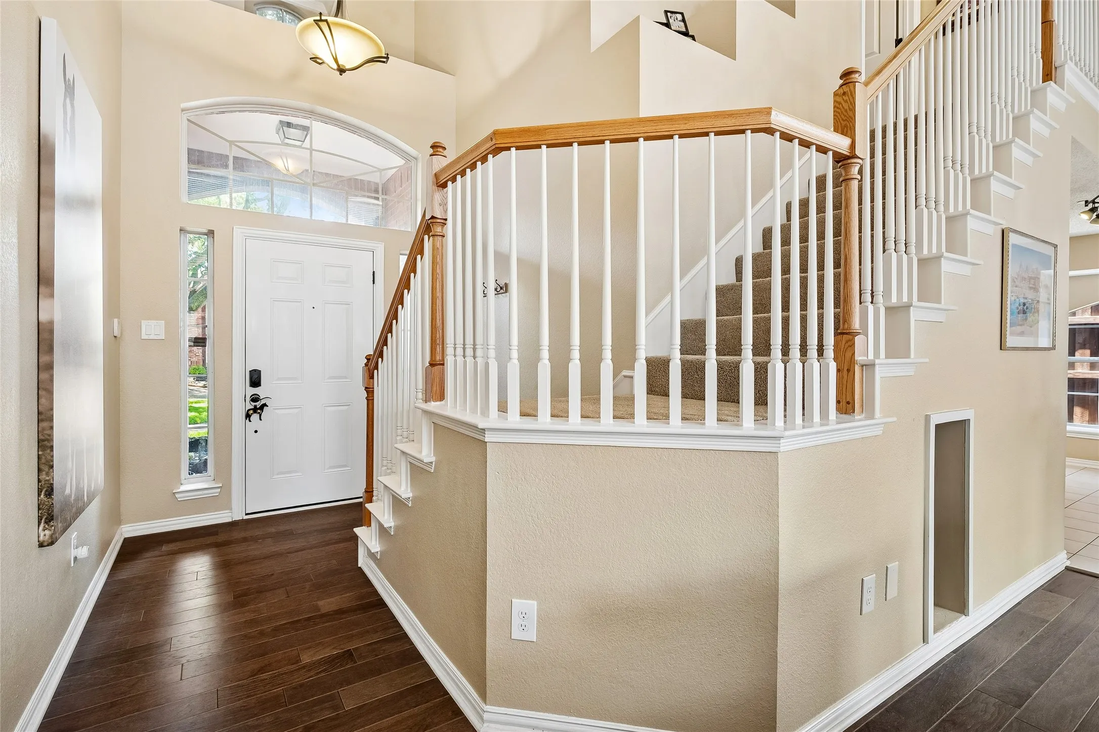 Grand entryway featuring wood-finish flooring, a white front door with sidelight and arched transom windows, and a staircase with white spindles and wood handrails