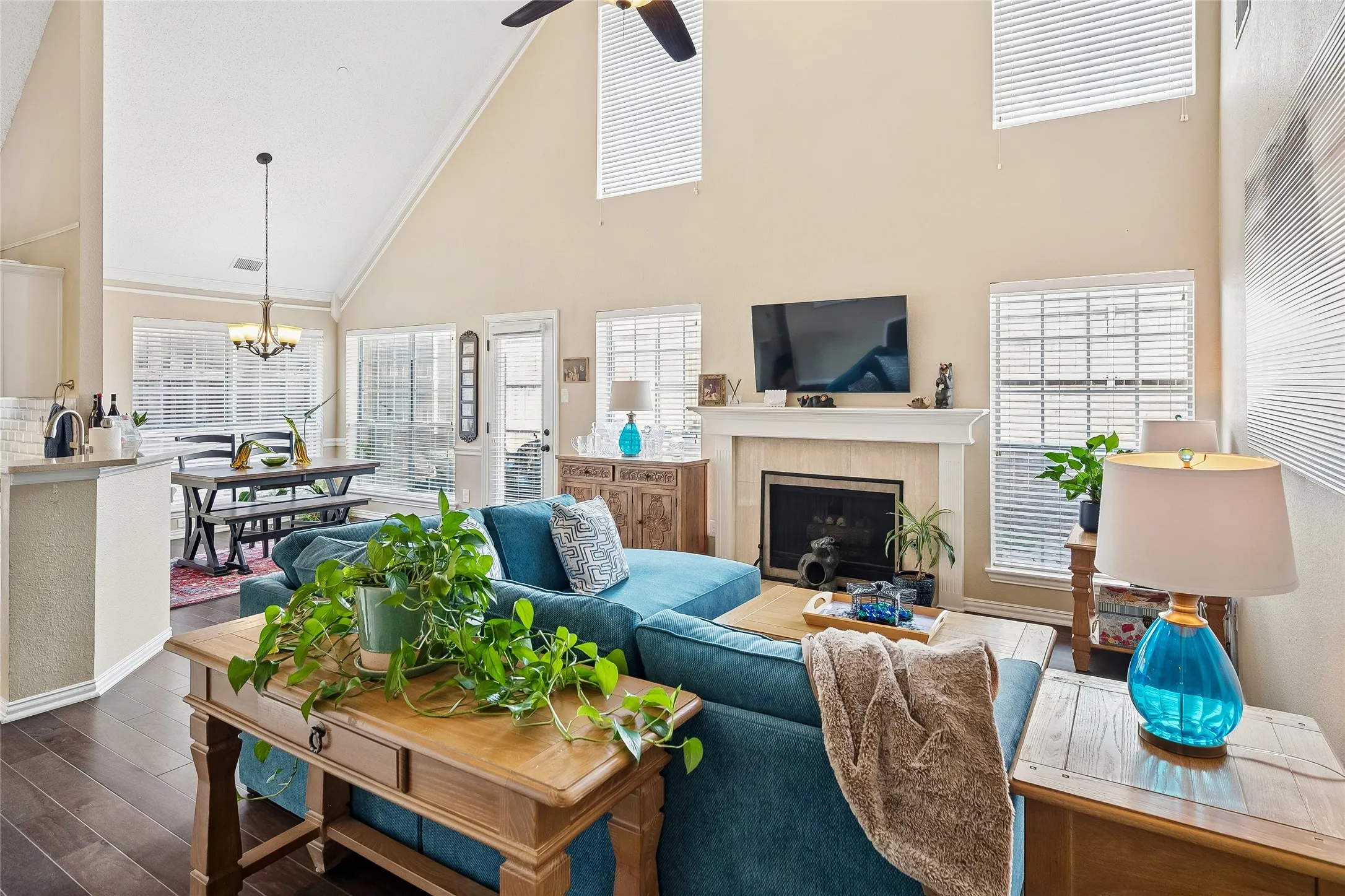 Vaulted ceiling living area featuring a fireplace with a stone surround, multiple windows with blinds, dark wood-finish flooring, and an open concept layout with a dining area