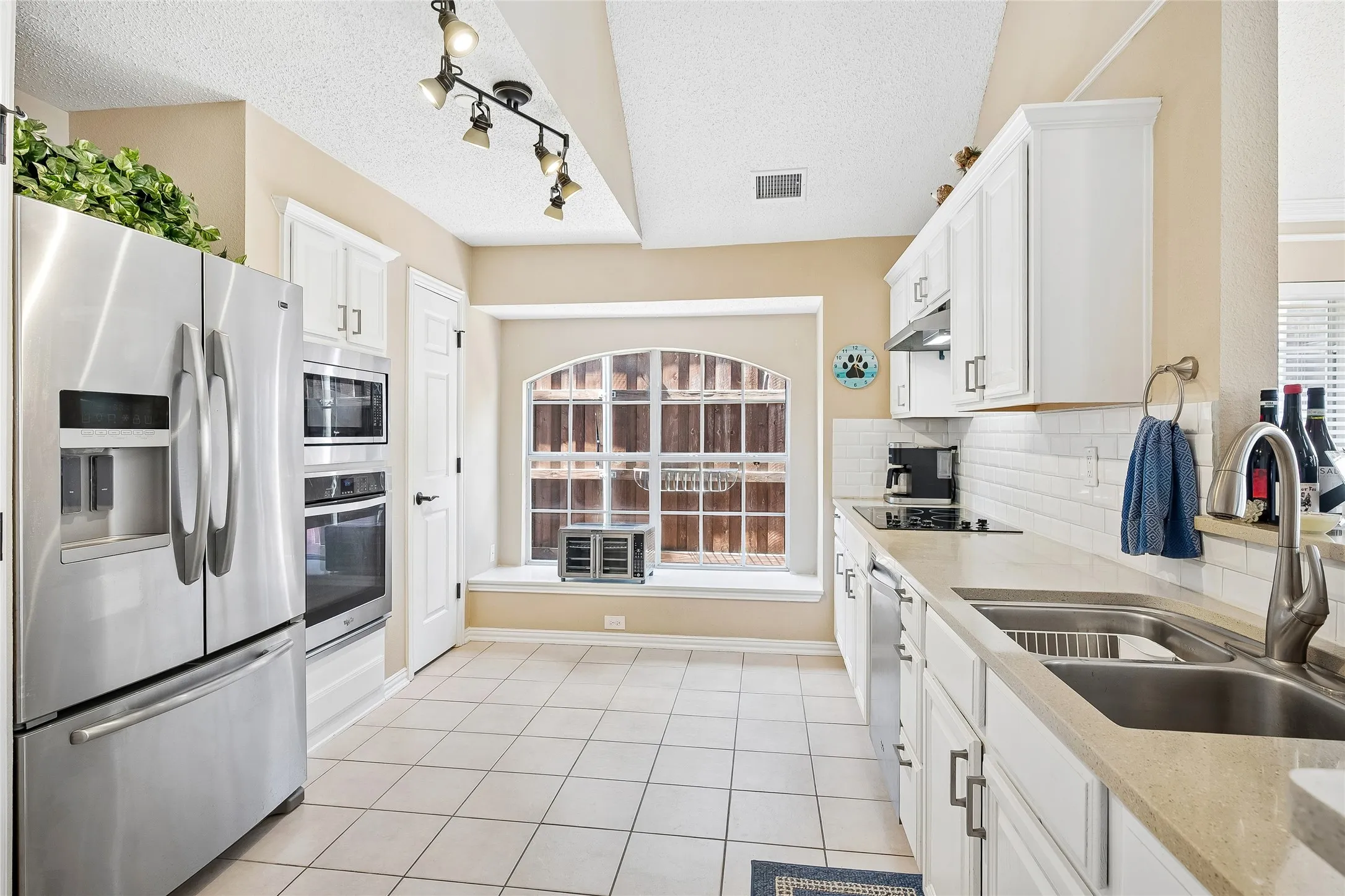 Kitchen featuring stainless steel appliances, white cabinetry, integrated sink, light-toned countertops, and an arched window
