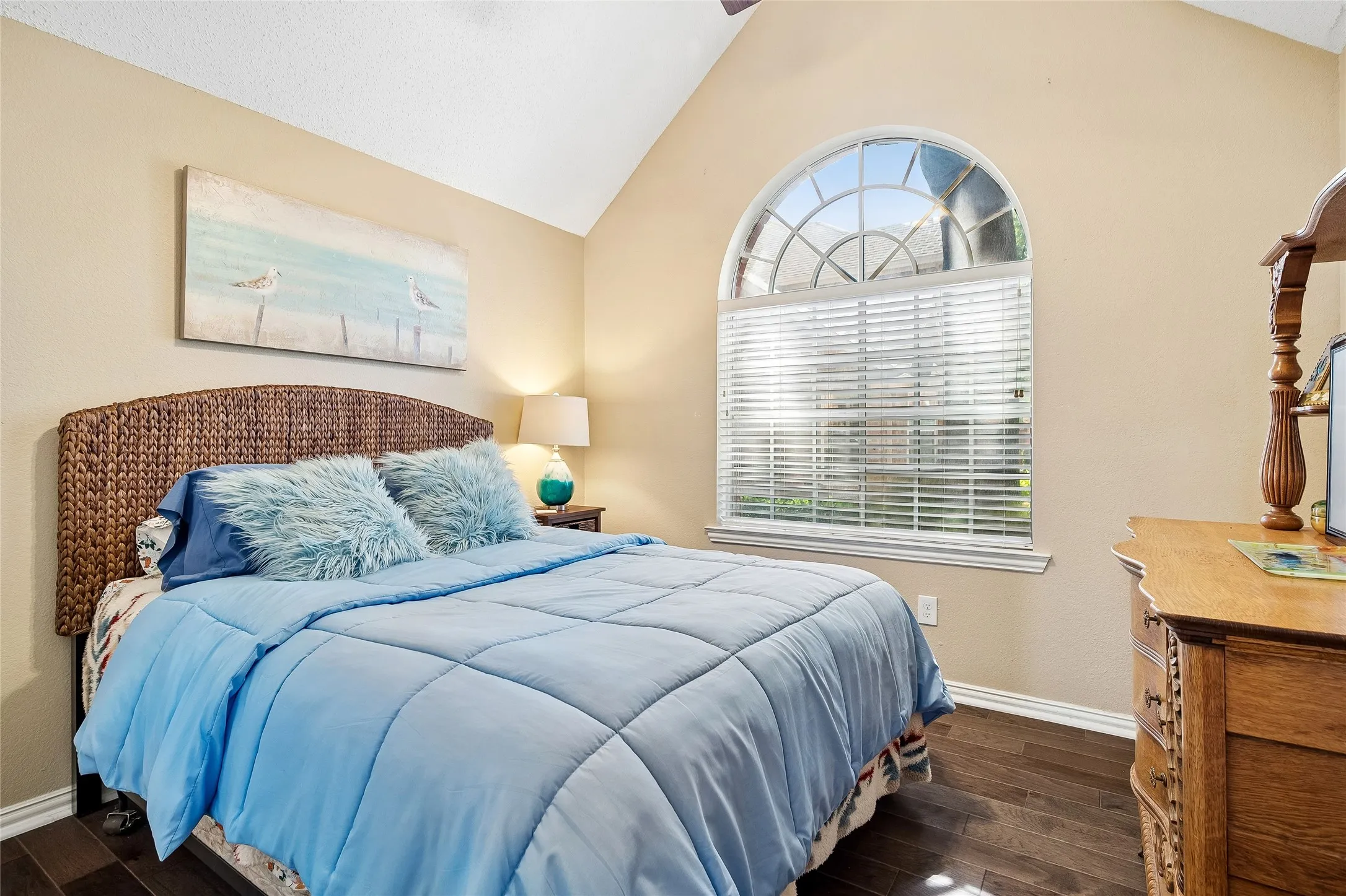 Vaulted ceiling with a ceiling fan, a large arched window with blinds, and wood-finish flooring