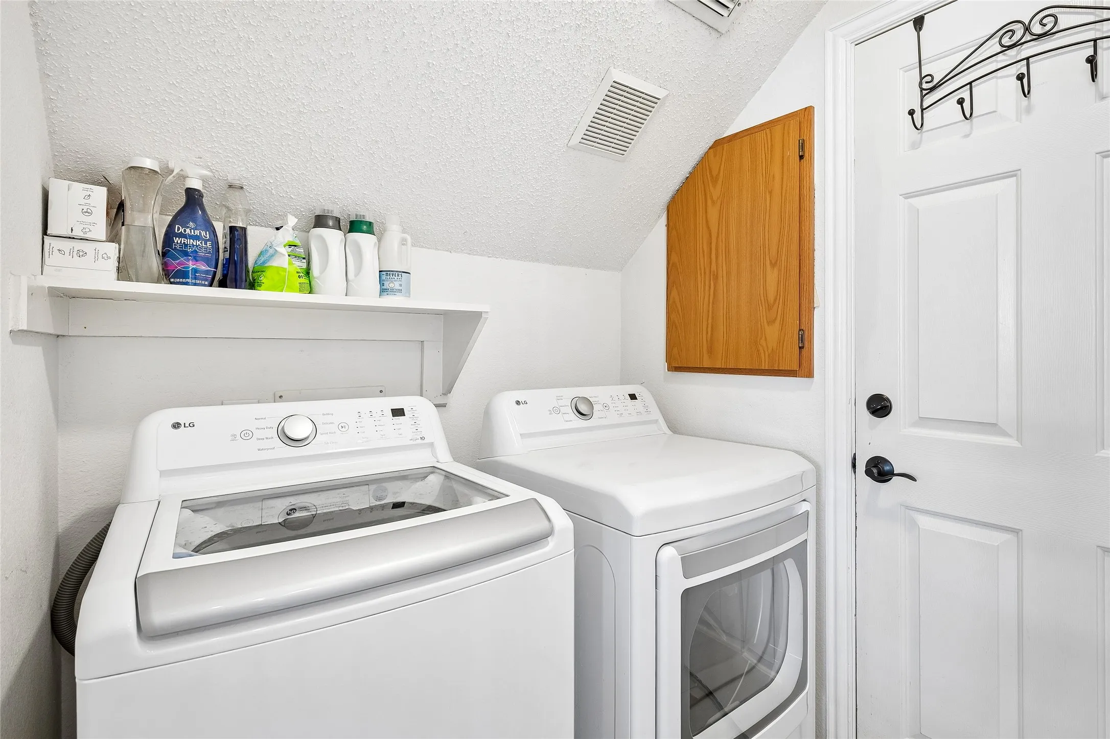 Dedicated utility area featuring a built-in wood-finish cabinet, white shelving, and a white paneled door with black hardware