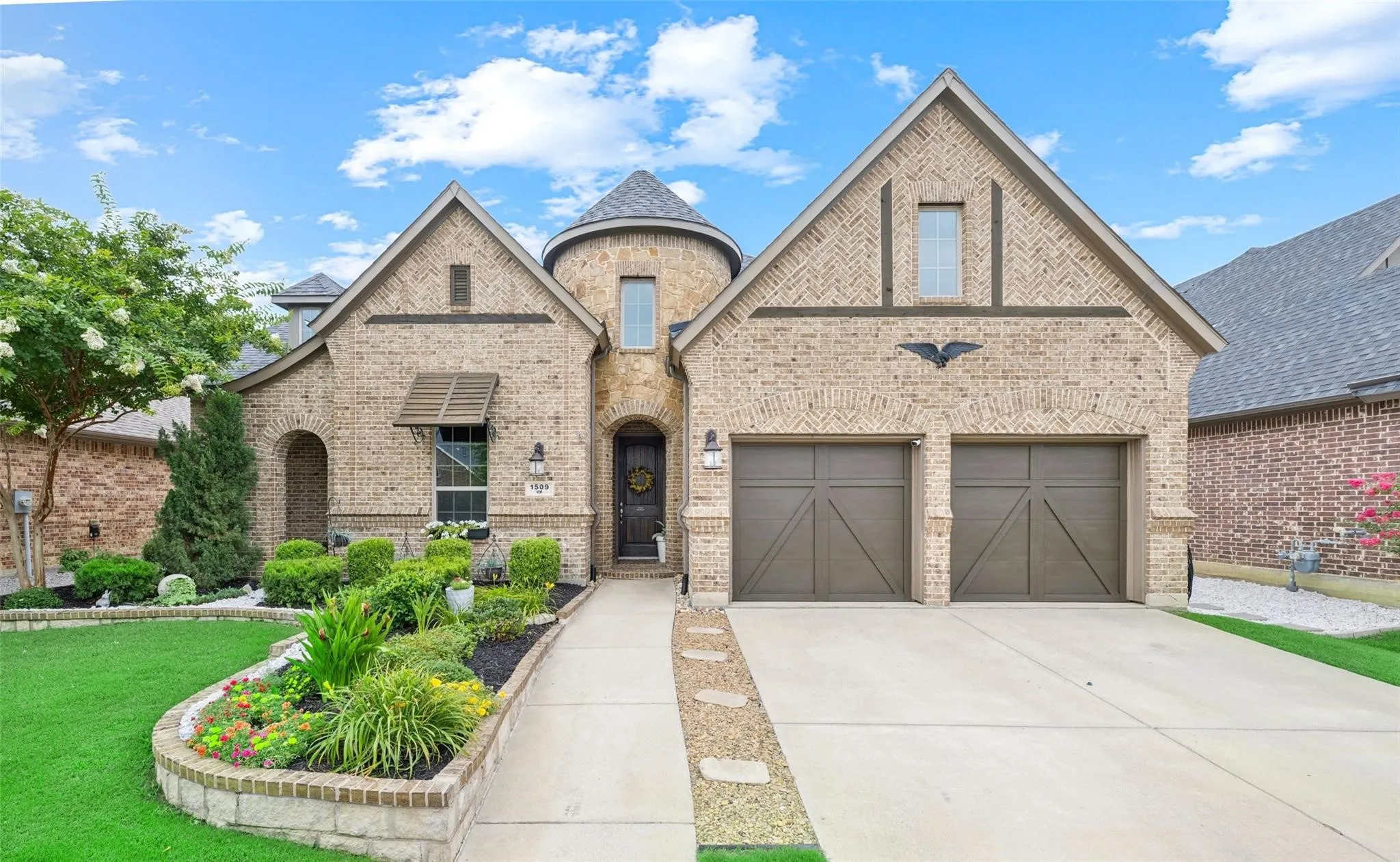 Brick exterior with a turret feature, attached two-car garage, and a manicured front lawn