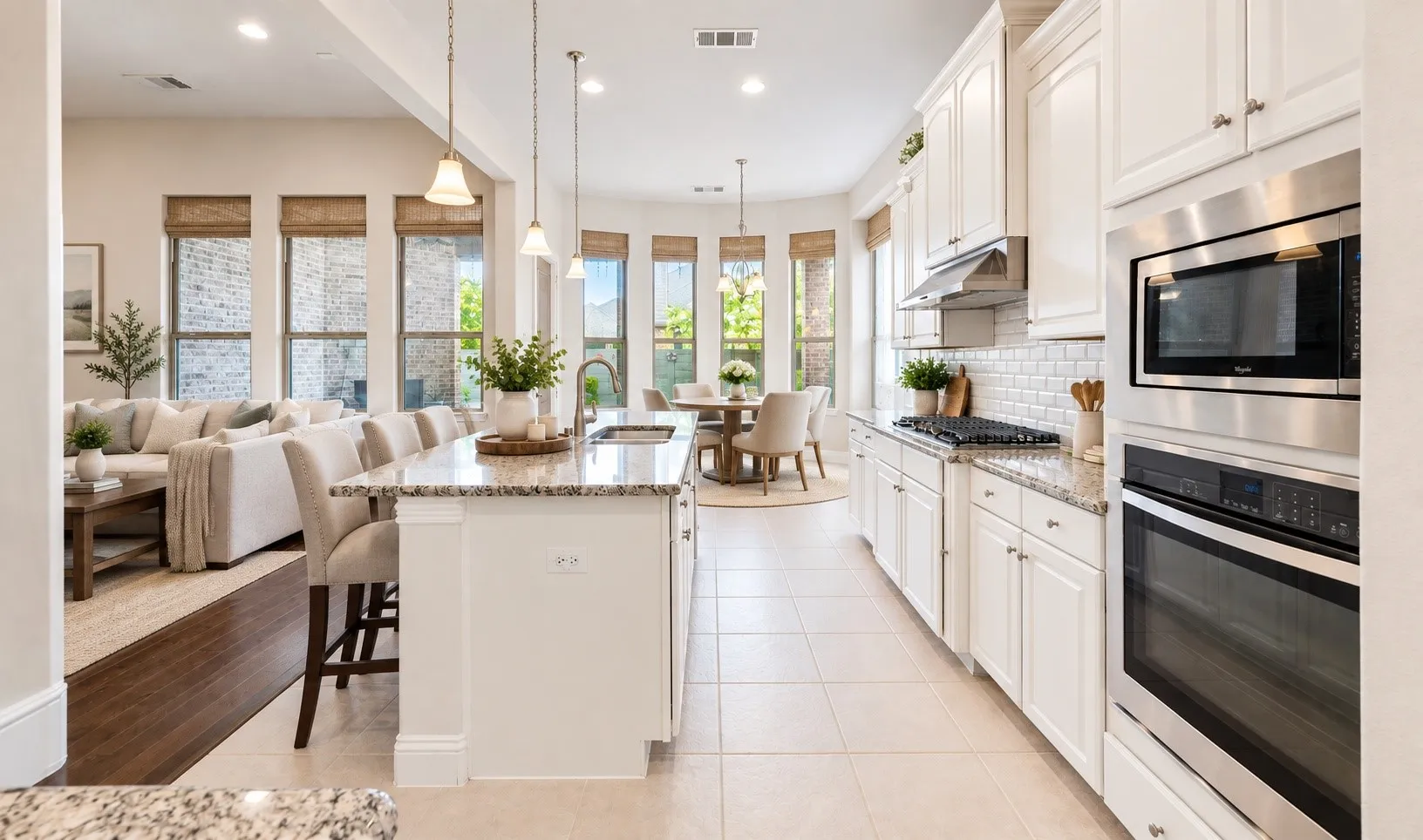 Open-concept kitchen featuring an island with pendant lighting, white cabinetry, integrated stainless steel appliances, and tile flooring *virtually staged*