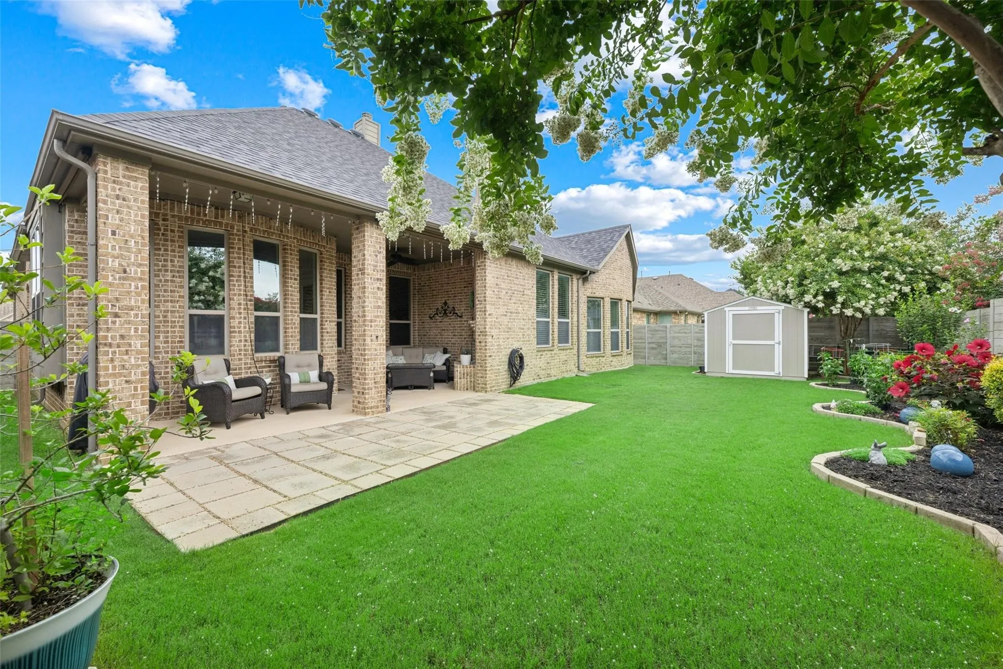 Brick exterior with a covered patio, extensive lawn, and a storage shed