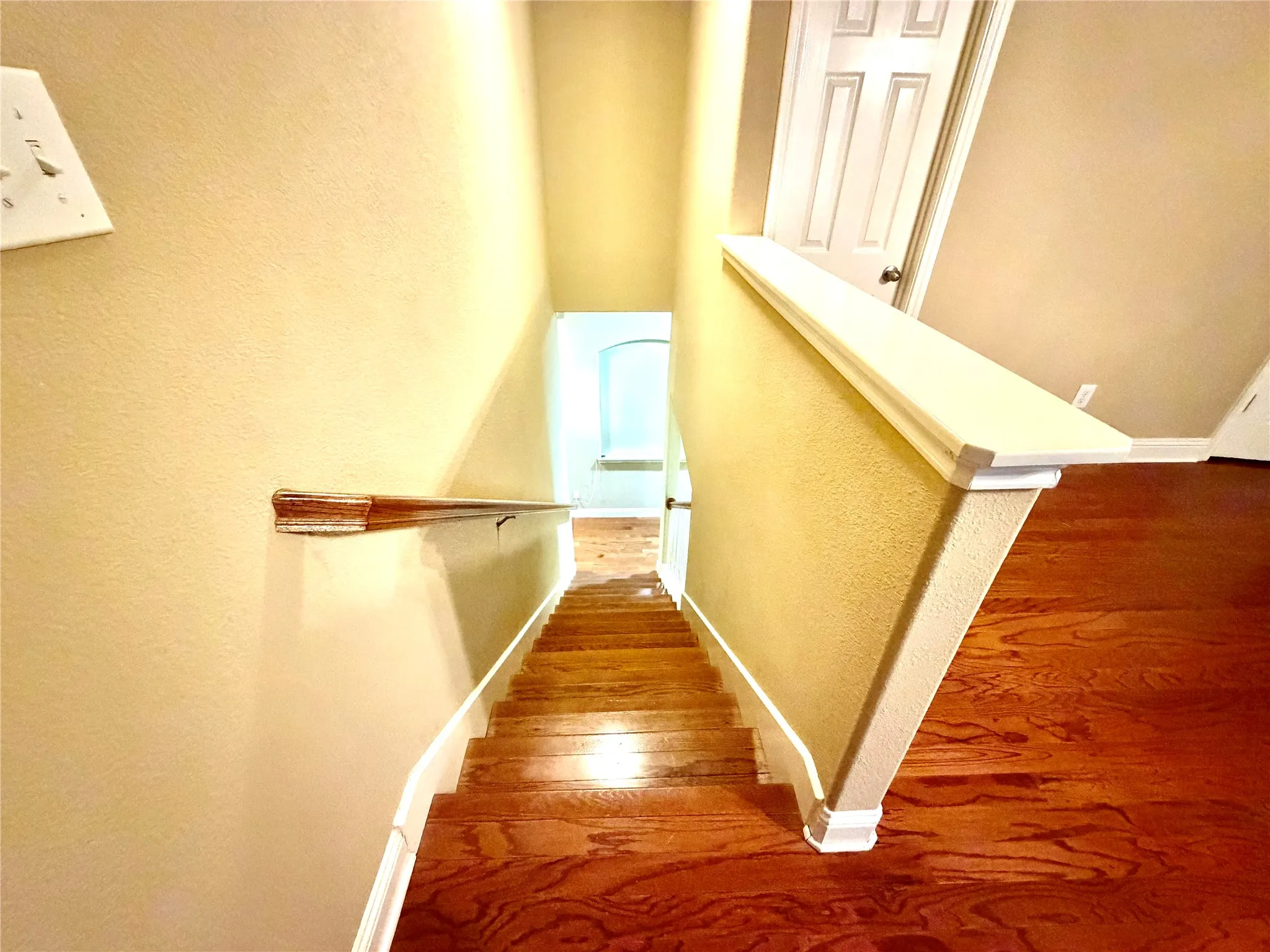 Staircase with wood-finish treads and risers, featuring a wood handrail and painted balustrade